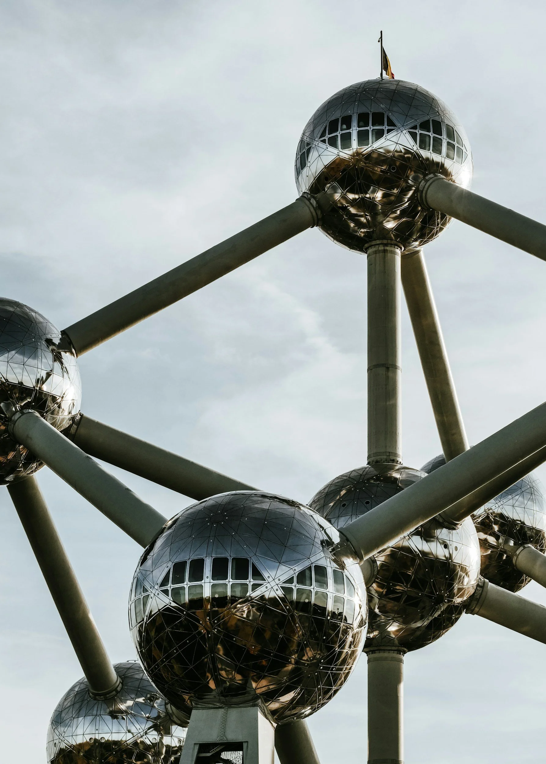 Close-up of the Atomium structure in Brussels, Belgium, featuring interconnected reflective metal spheres and supporting beams against a gray sky.