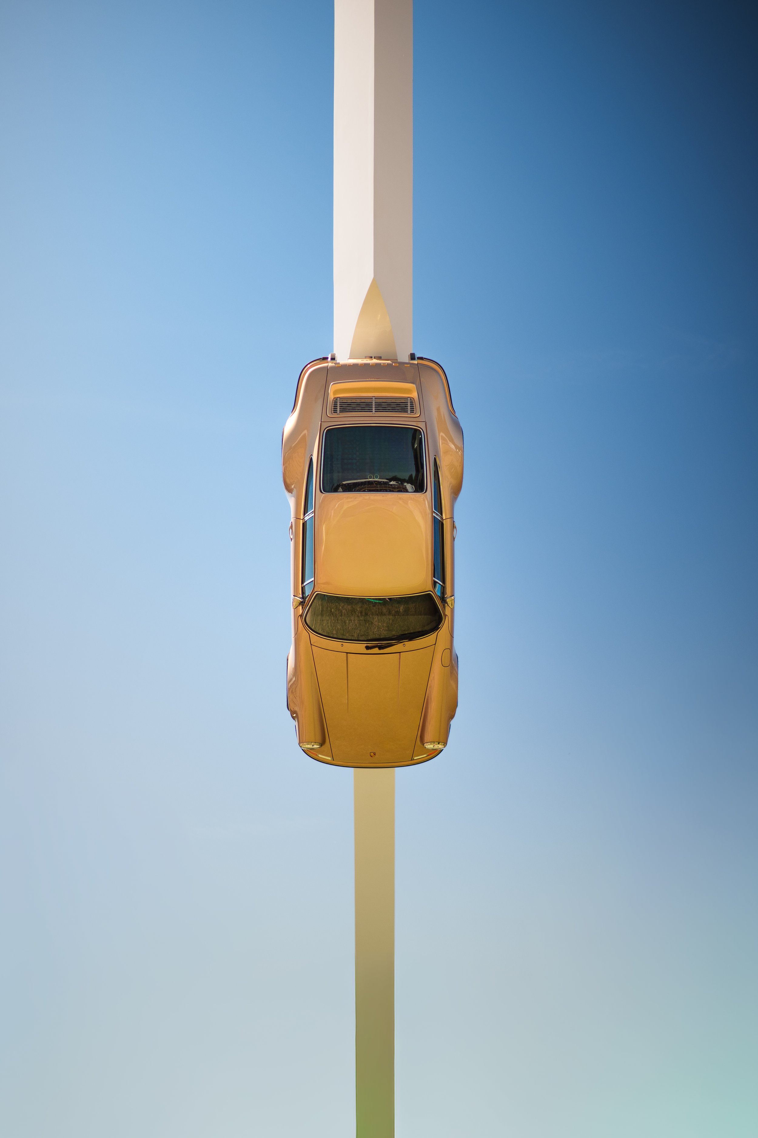 A yellow sports car seen from above, driving on a straight road under a clear blue sky.