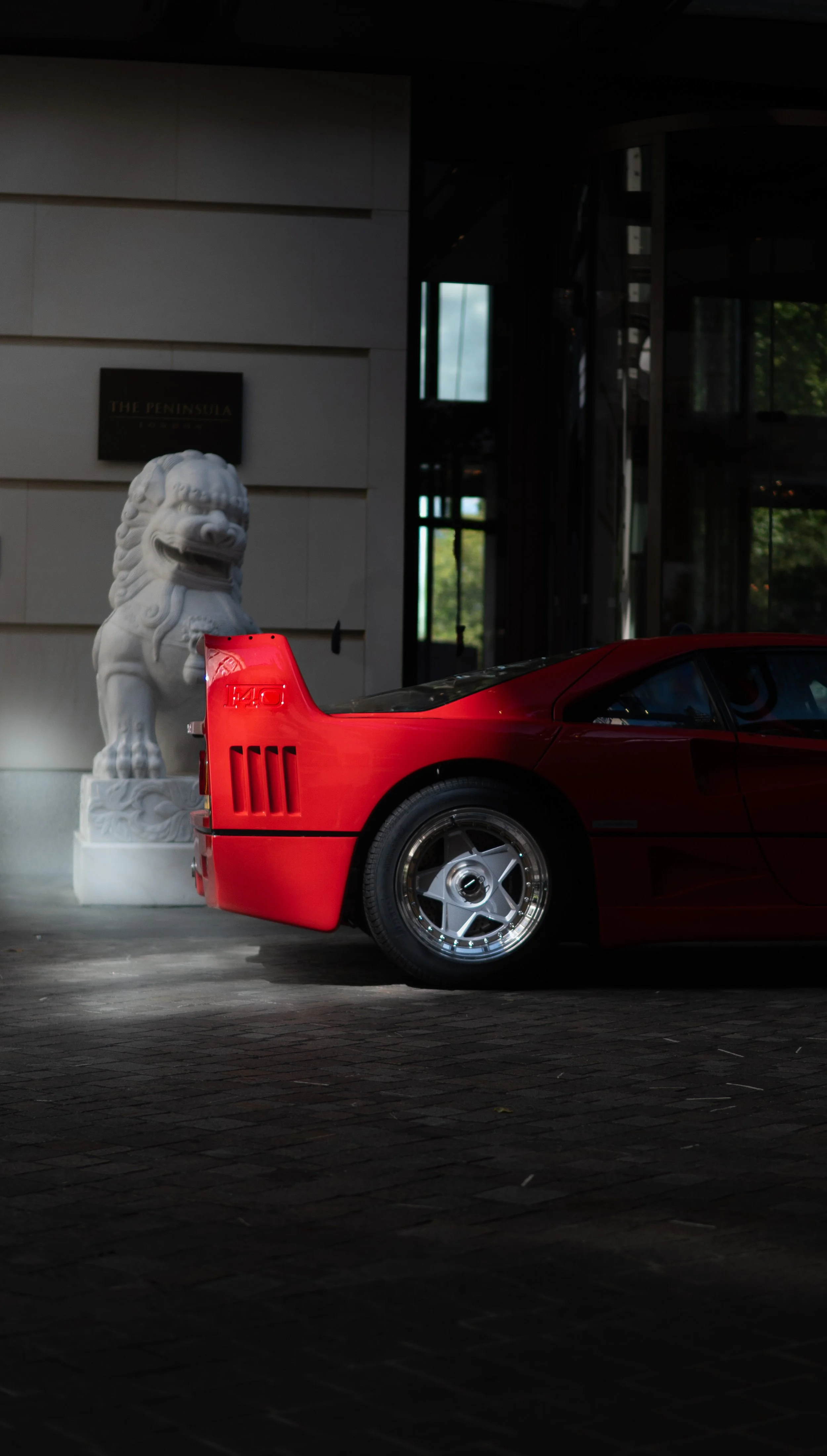 A Ferrari F40 parked beside a white stone lion statue outside the 'The Peninsula' in Mayfair.