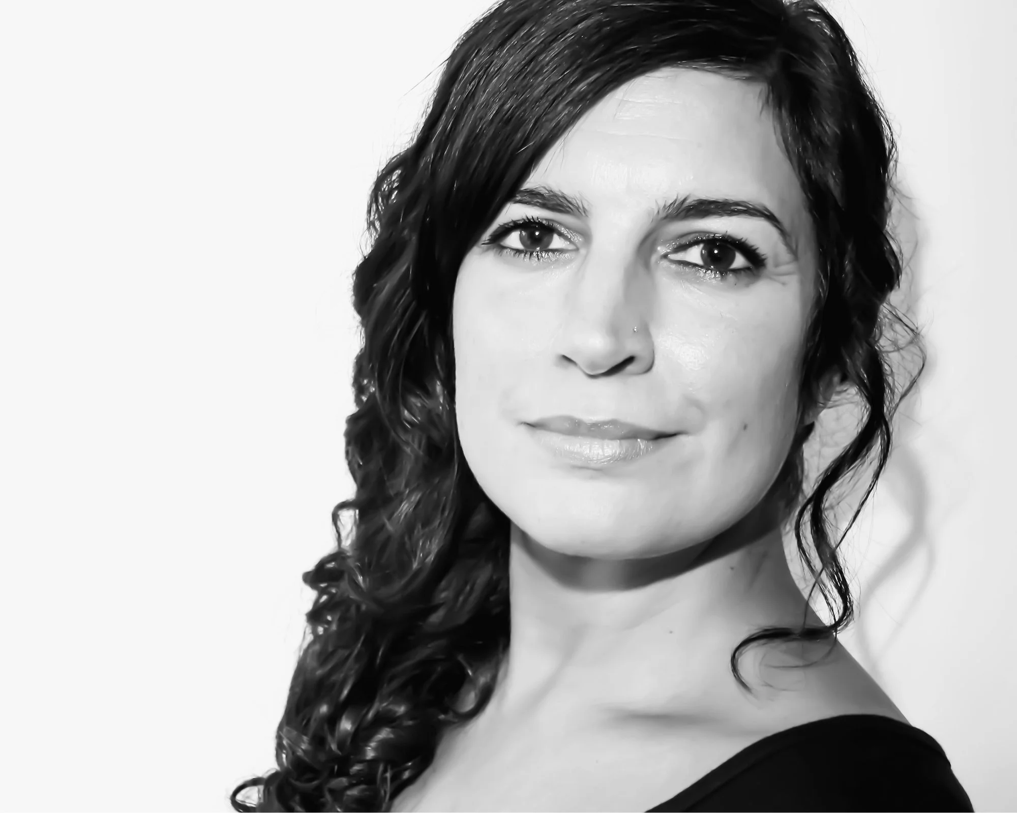 Black and white headshot of Amelia. She has dark wavy hair, facing the camera with a calm expression.