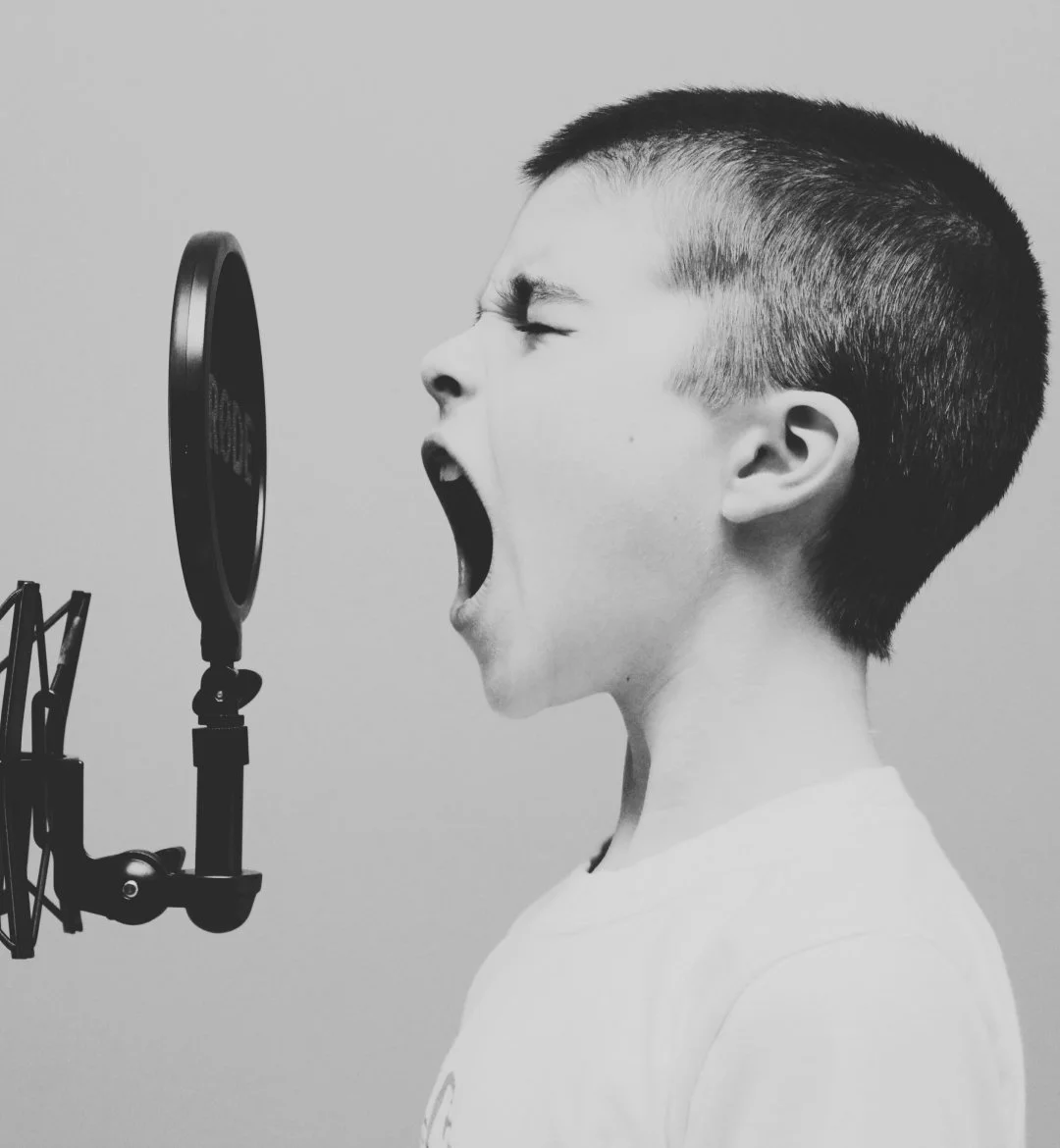 a young boy sining or shouting into a studio microphone