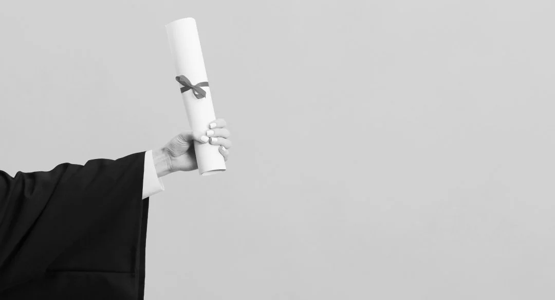 An outstretched arm in graduate robe holding out a scroll or diploma