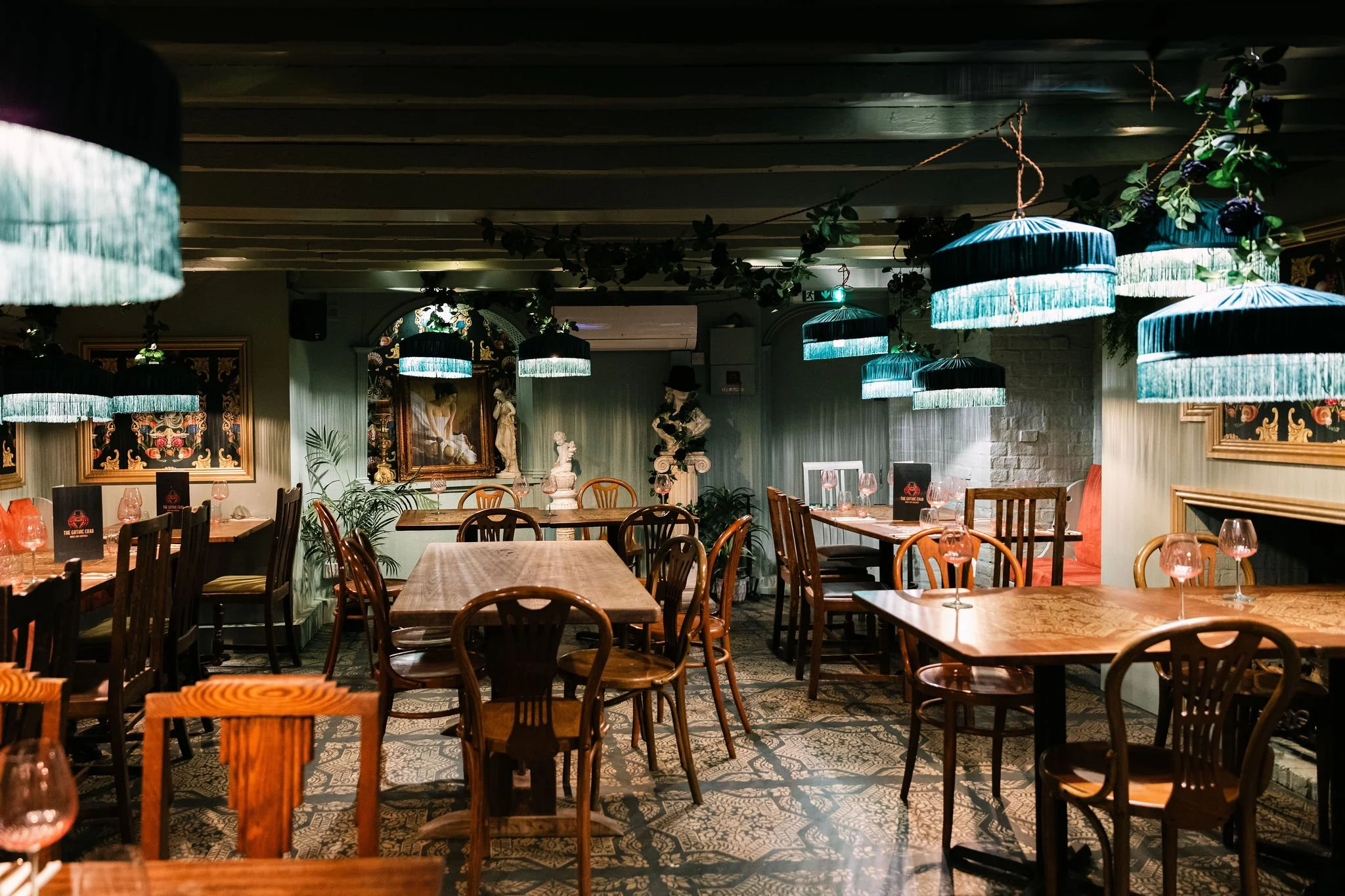 Interior of a restaurant with wooden tables, chairs, blue hanging lamps, and decorative artwork on the walls.
