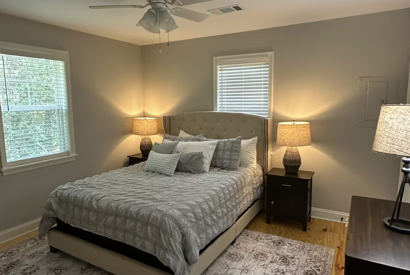 Bedroom with a bed, nightstands, lamps, windows, and a ceiling fan.