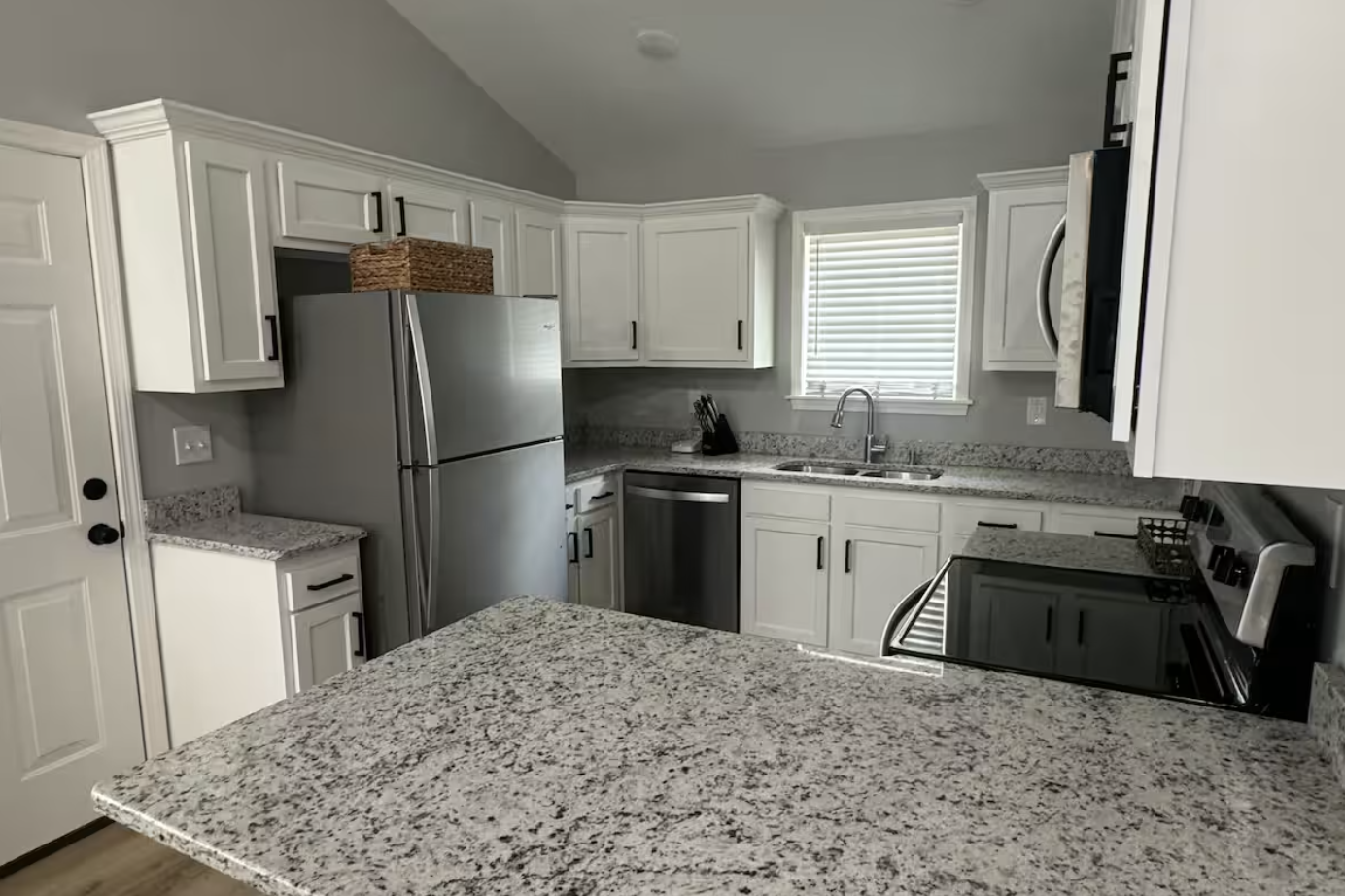 Modern kitchen with white cabinets, granite countertops, stainless steel appliances, and a window above the sink.
