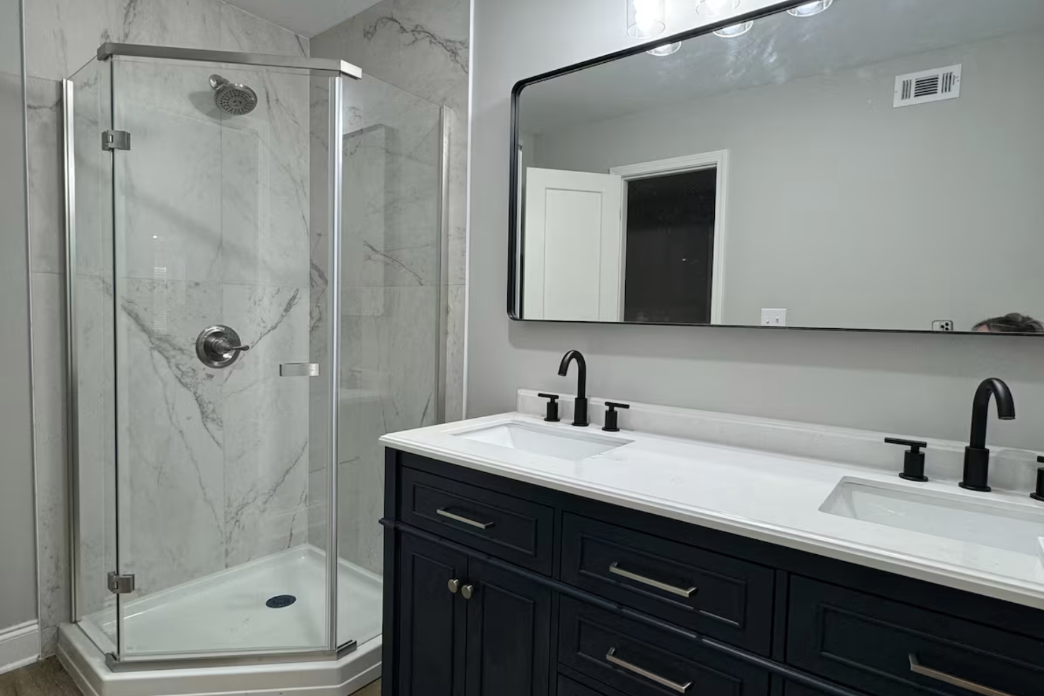 Modern bathroom featuring a glass enclosed shower with marble walls and a black vanity with two sinks, black faucets, and a large mirror.