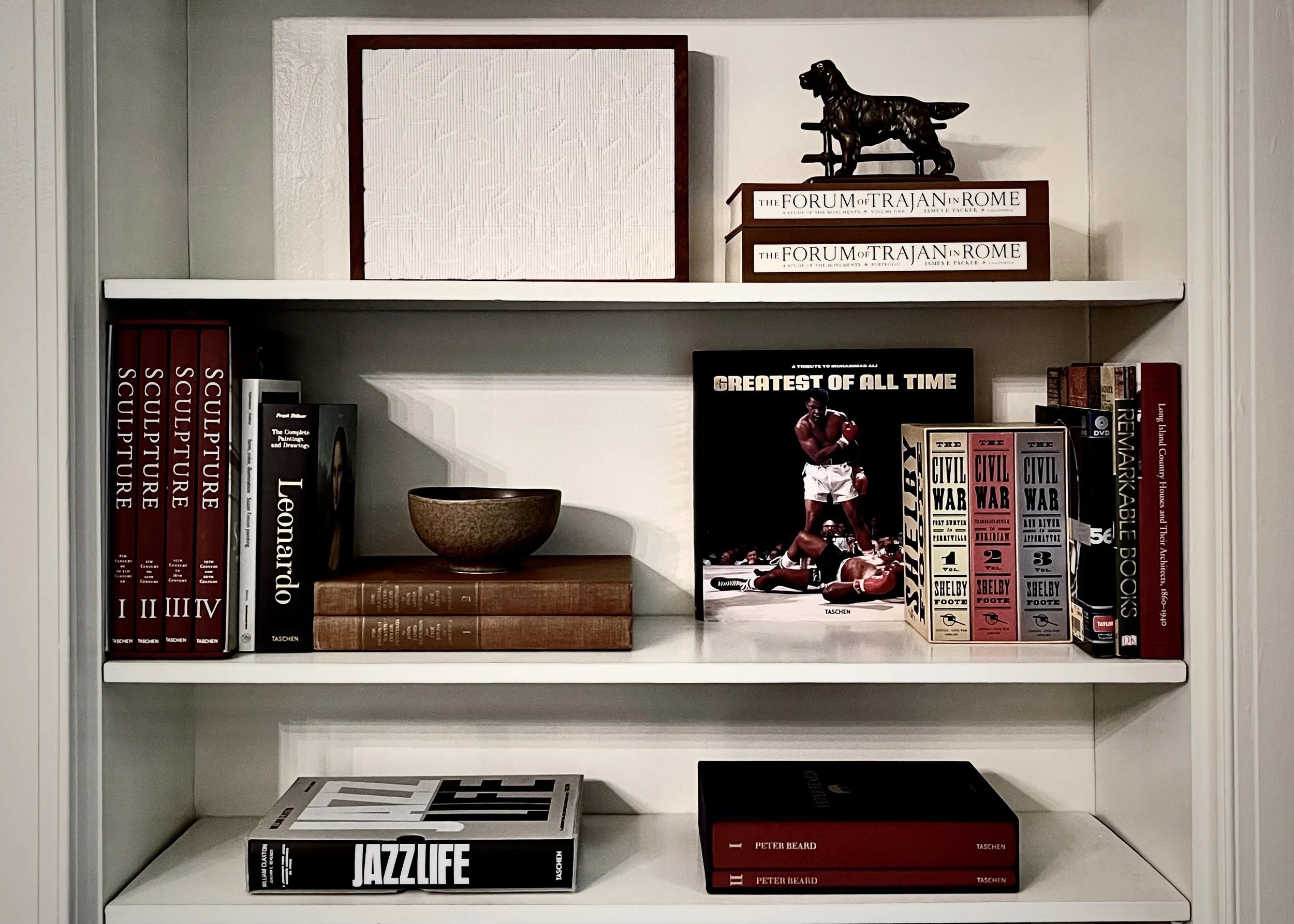 Curated bookshelf with art books, sculptural objects, and layered materials in painted wood built-in, residential interior styling by Alexander Mann