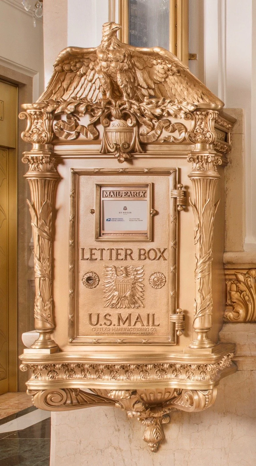 Ornate gold letter box with eagle crest and classical detailing in historic interior