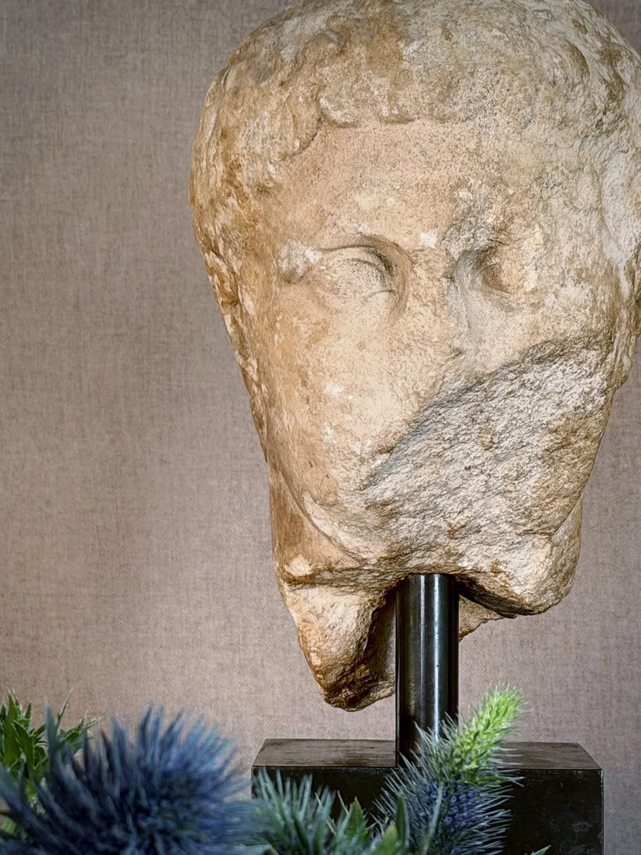 Ancient Roman marble head sculpture on stand against textured wall, residential interior detail