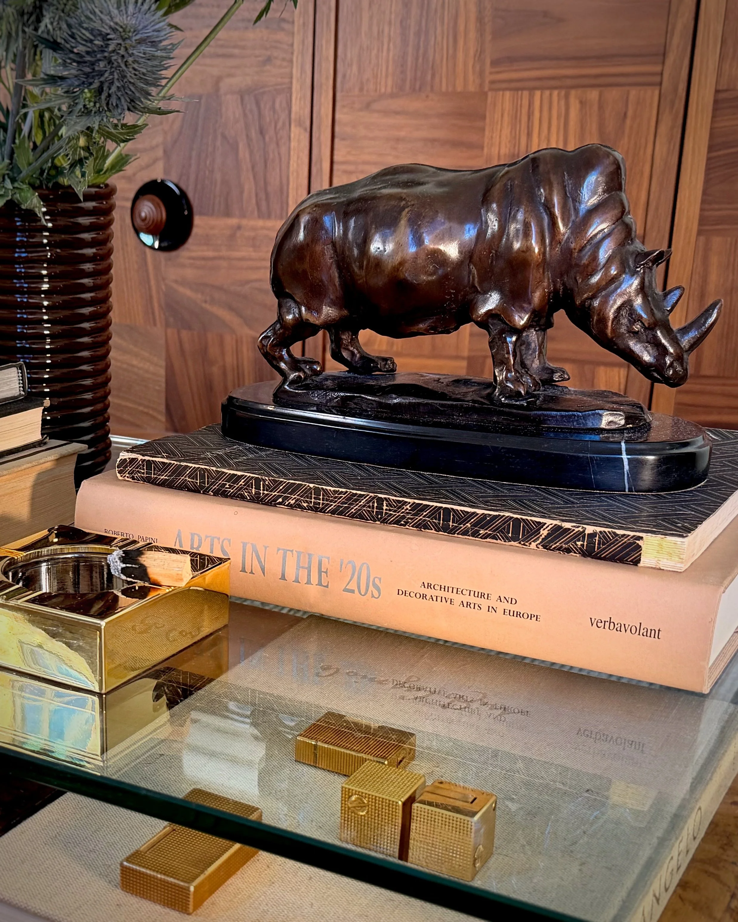 Styled vignette with bronze rhinoceros sculpture, Art Deco books, vintage lighters, and glass coffee table in residential interior by Alexander Mann