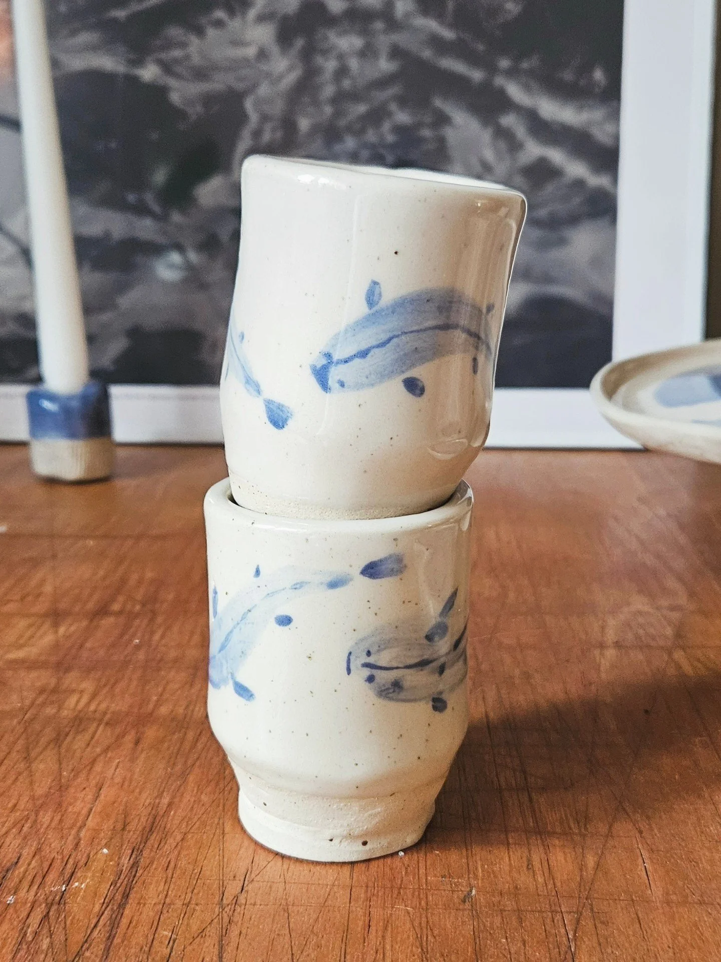 Kaksi käsityönä tehtyä keramiikkamukia, joissa on sinisiä vesiaiheisia kuvioita, asetettuna päällekkäin wooden pöydällä.
