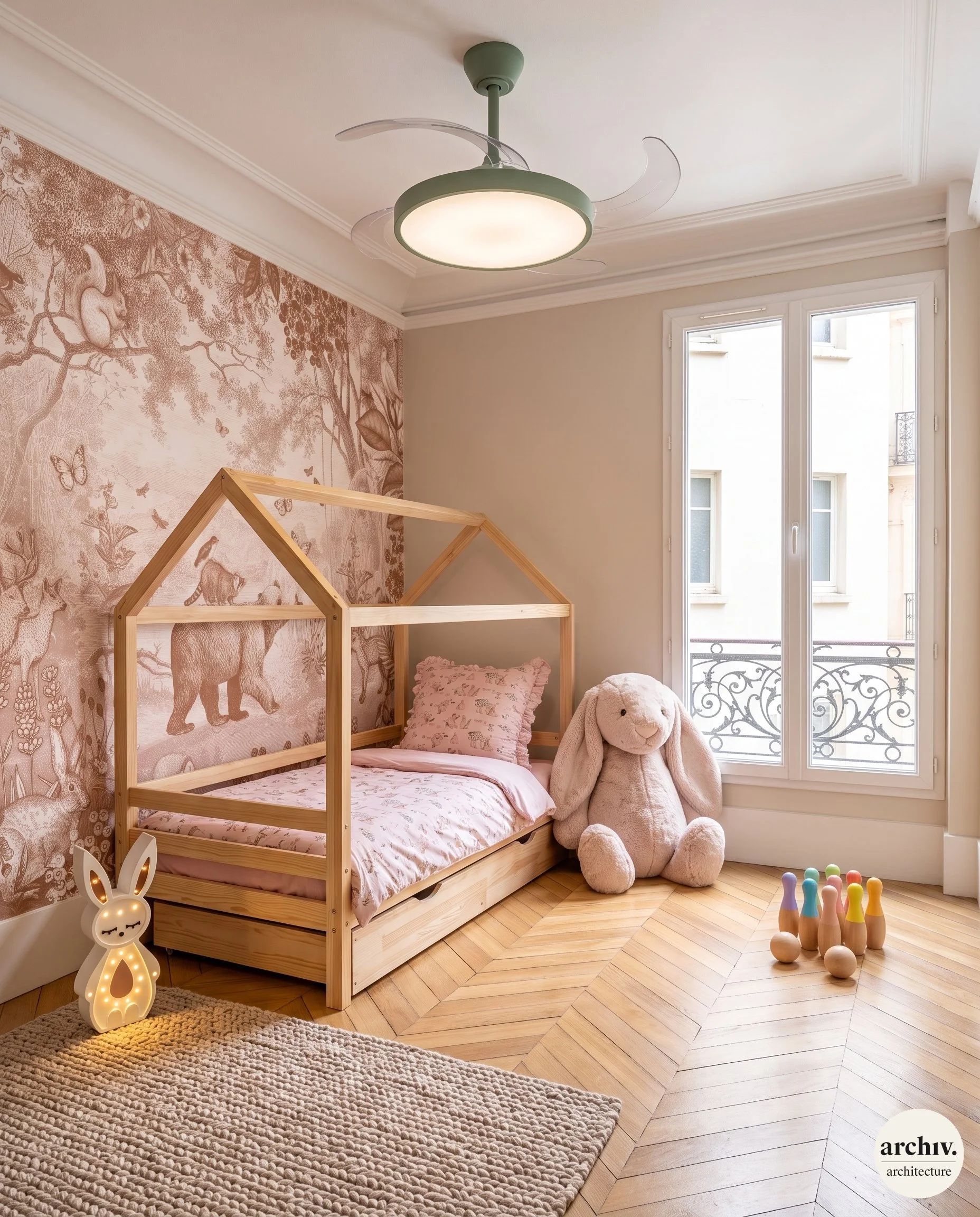 Chambre d'enfant avec un lit en forme de cabane en bois, coussins et grand doudou, mur avec papier peint à motifs d'animaux, jouets bowling sur le sol, ventilateur de plafond