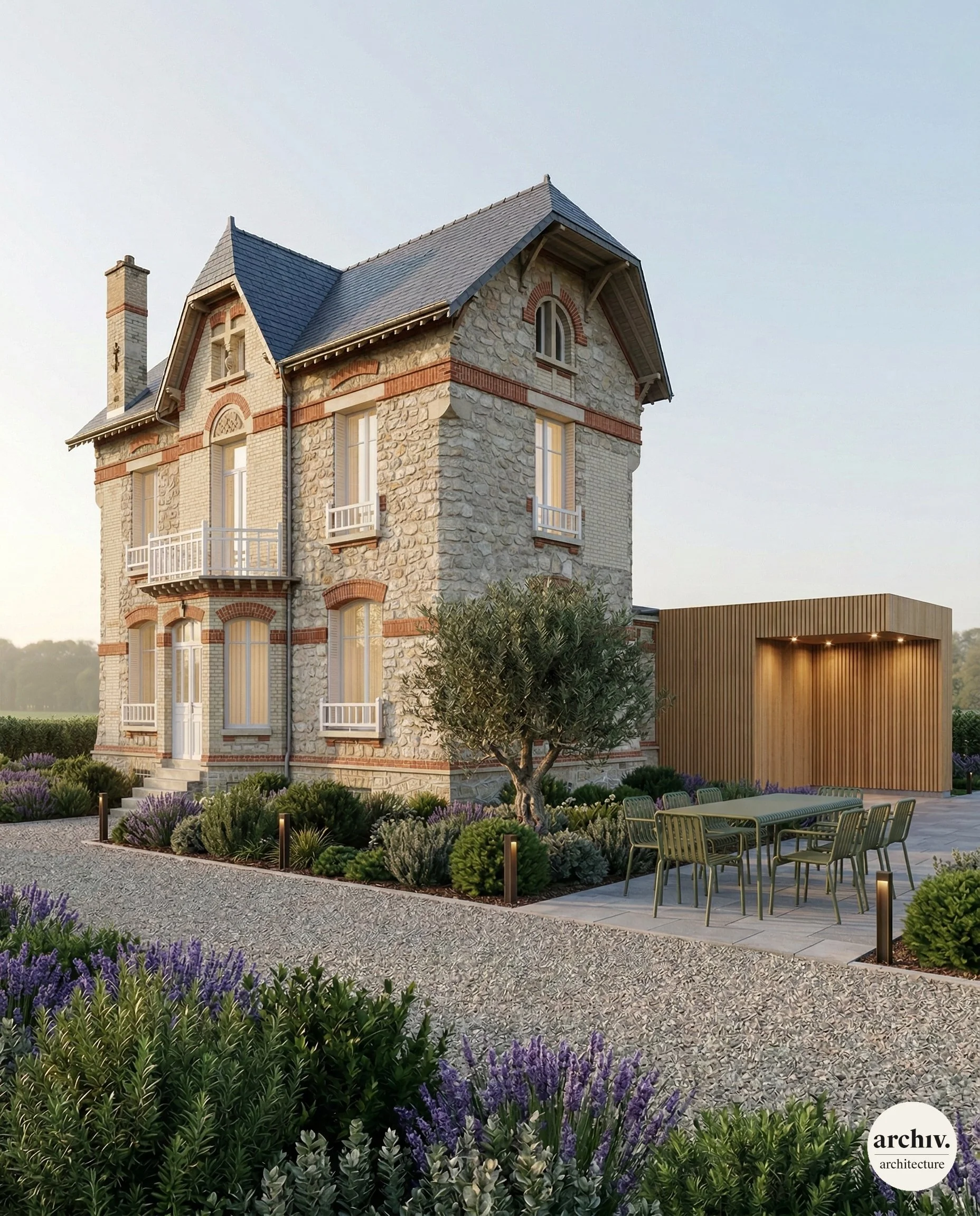 A large, multi-story stone house with a turret, surrounded by landscaped garden with purple flowers, bushes, and a gravel pathway. There is an outdoor table and chairs on a patio and modern lighting. Reims.
