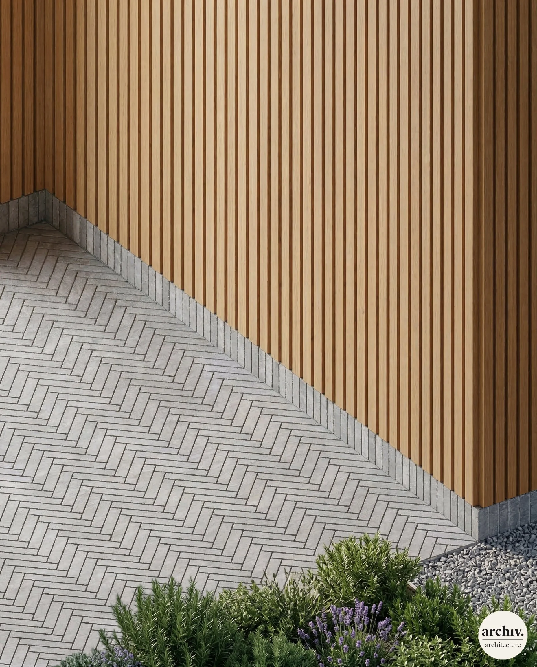 Close-up view of an outdoor corner with vertical wooden slat wall, grey herringbone paving, and green plants with purple flowers at the bottom right corner. Réemploi briques anciennes extension maison. Reims.