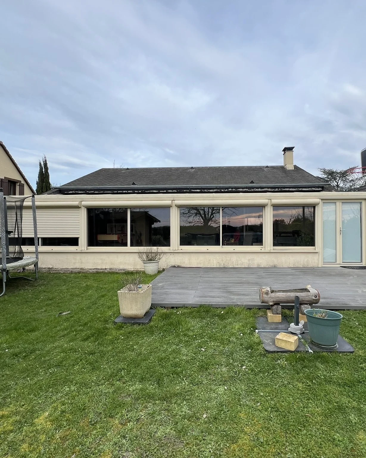 Maison en arrière-plan d'une véranda, pelouse et terrasse en bois à l'avant.