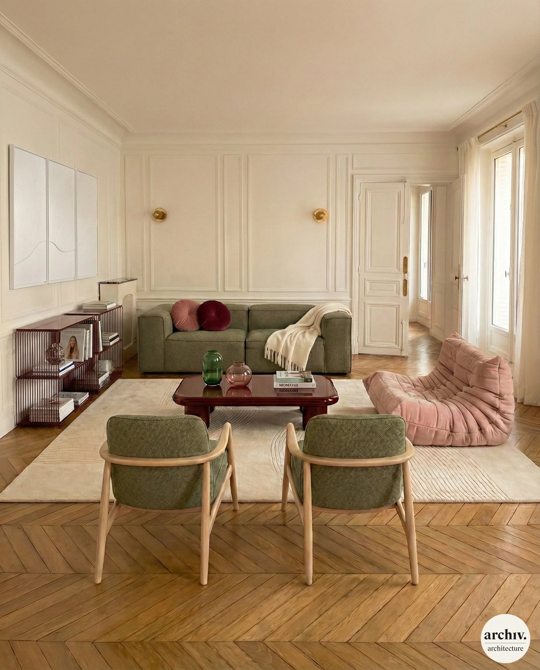 Haussmann living room with a green sofa, a pink armchair, two green armchairs, a wooden coffee table with vases and books, a light-colored area rug, built-in shelves with books, white walls with decorative molding. Paris.