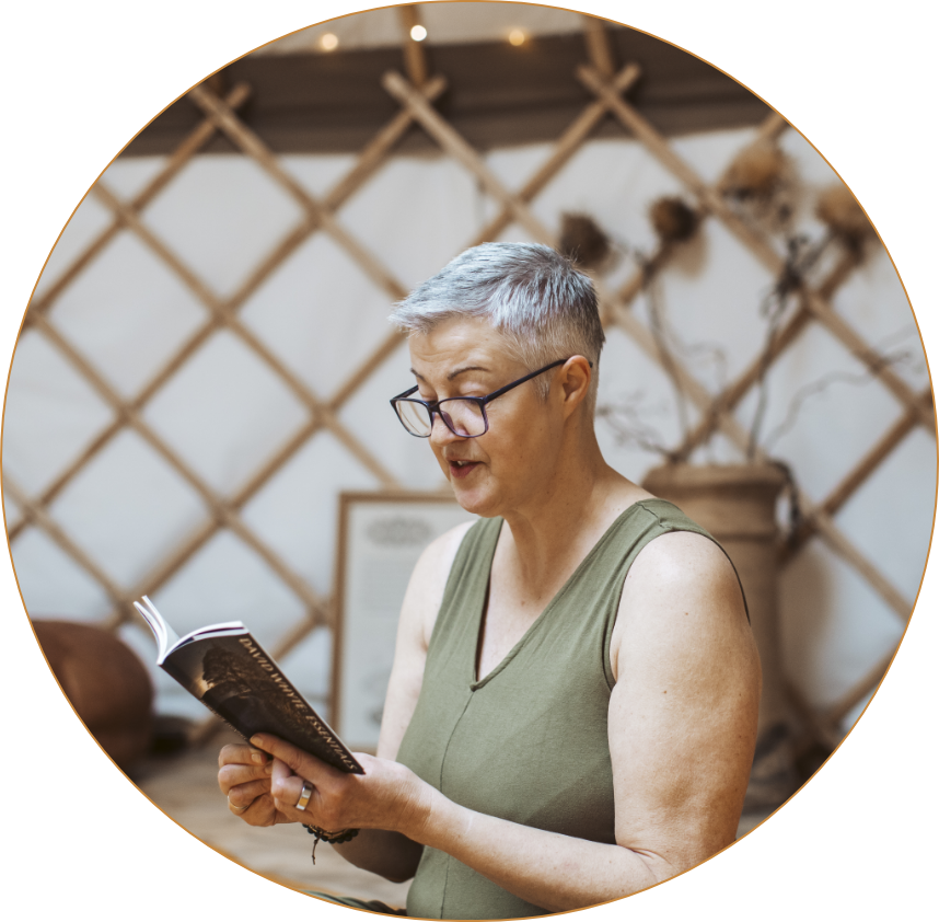A woman with short gray hair, glasses, and a sleeveless green top reading a book indoors.