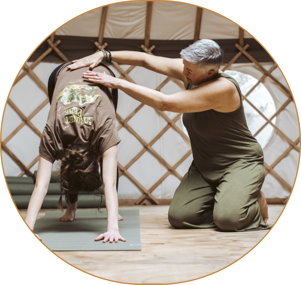 A woman practicing yoga in a yurt with a yoga instructor assisting her in a forward bend stretch.