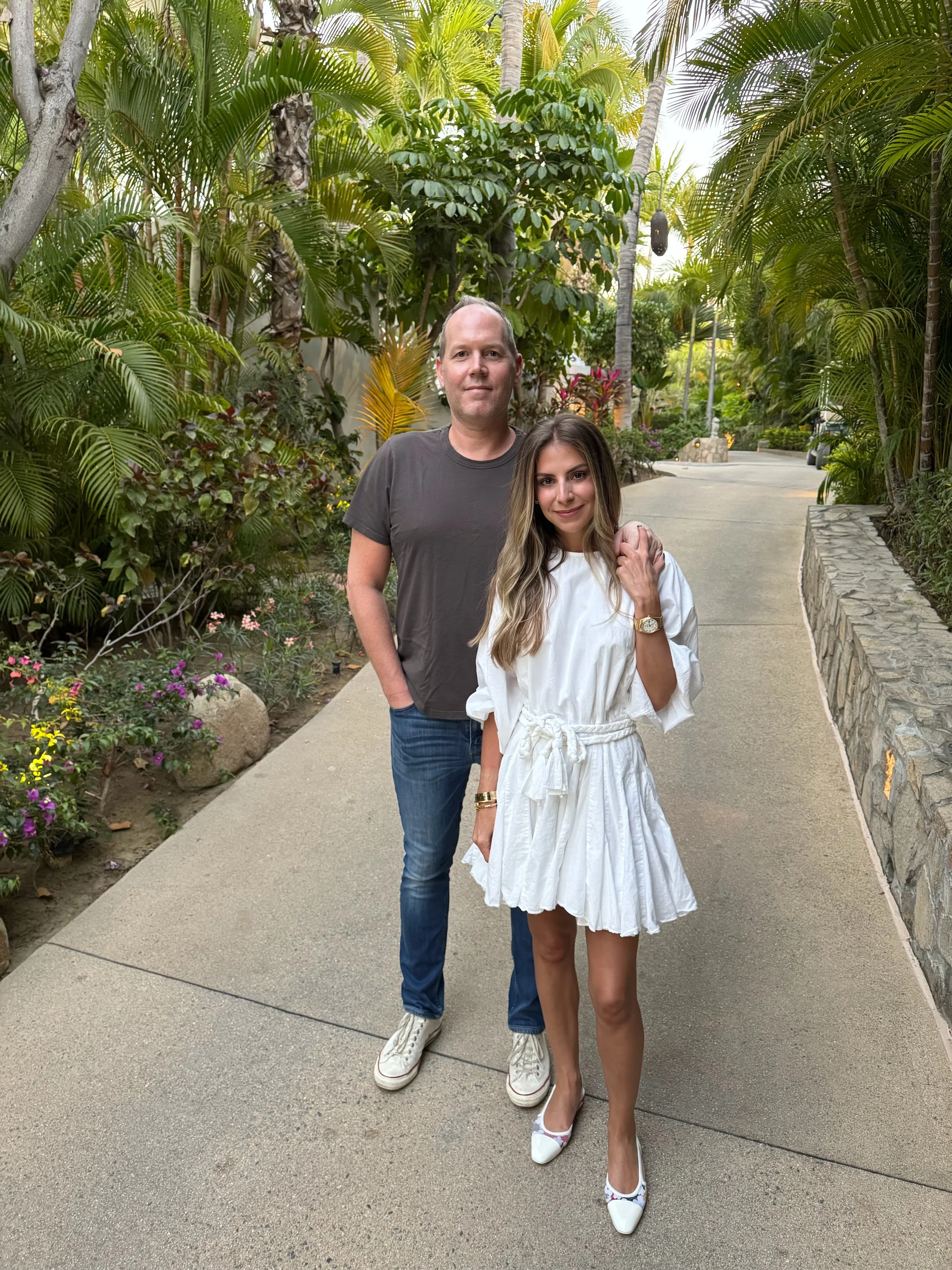 A man and woman standing on a paved path surrounded by lush tropical plants and trees.