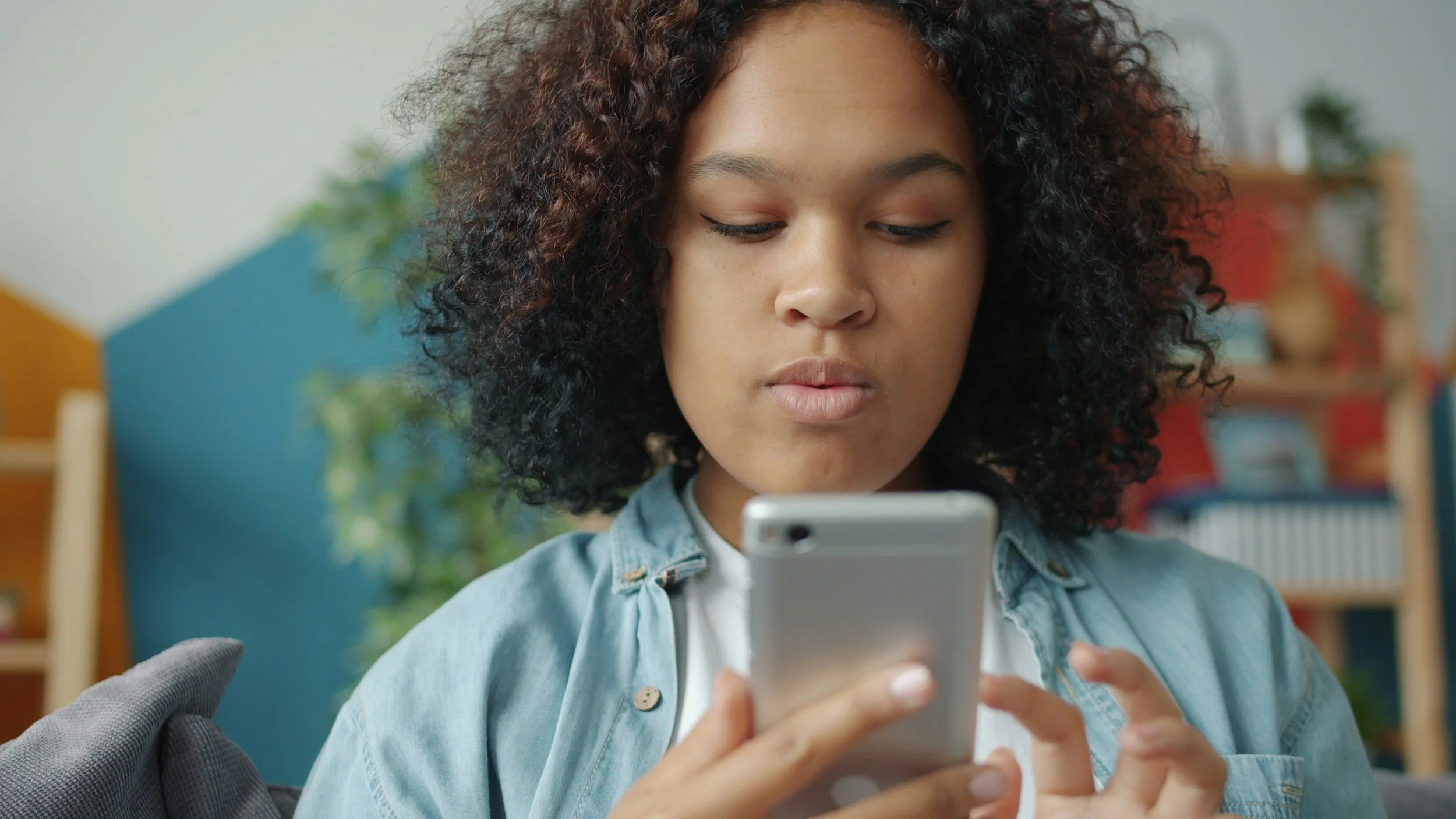 A young woman with curly hair looking at her smartphone indoors.