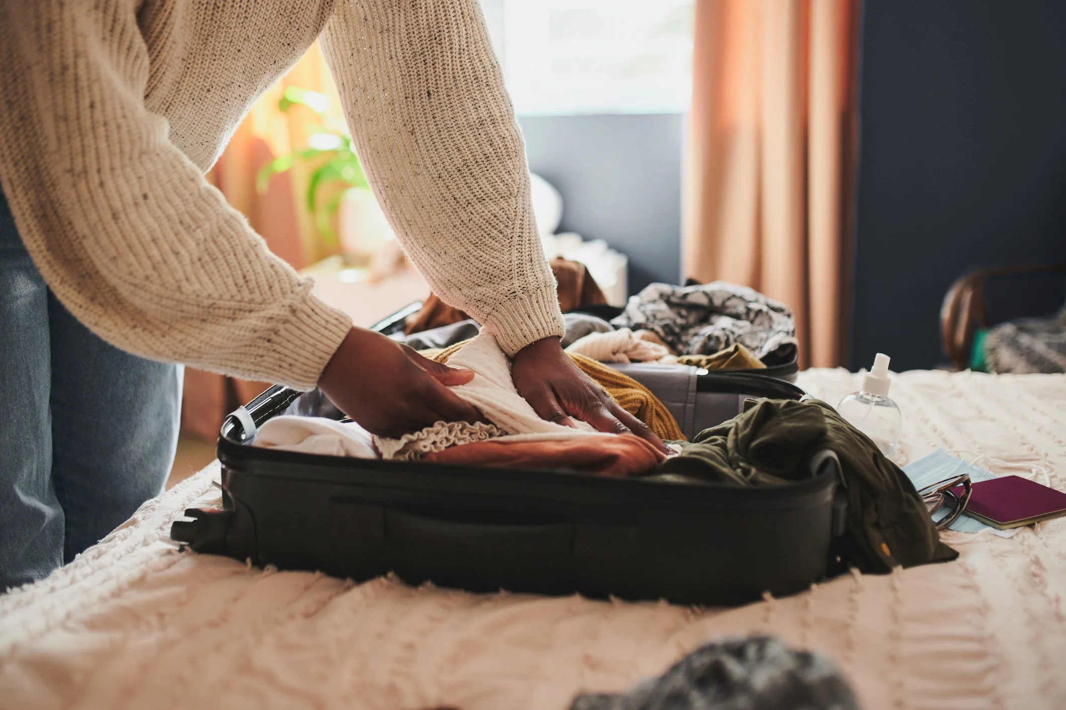 Person packing clothes into a suitcase on a bed.