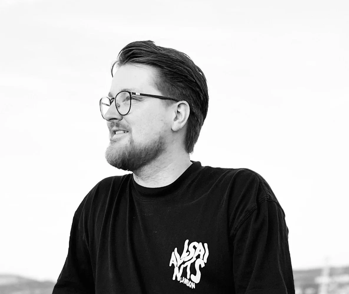 Side profile of a smiling man with glasses and a beard, wearing a black T-shirt with white text.