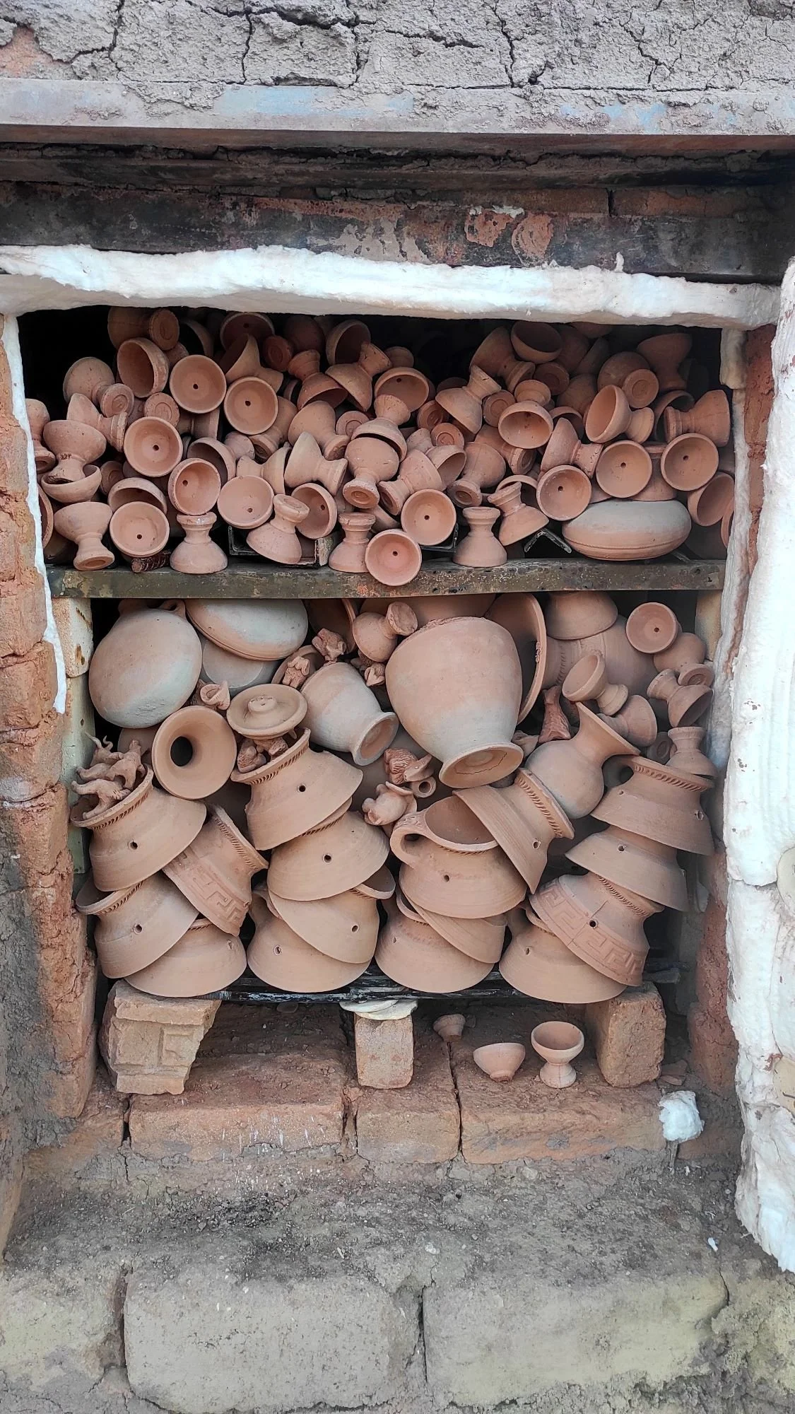 A collection of unglazed terracotta pottery pieces stored in a brick oven or kiln.