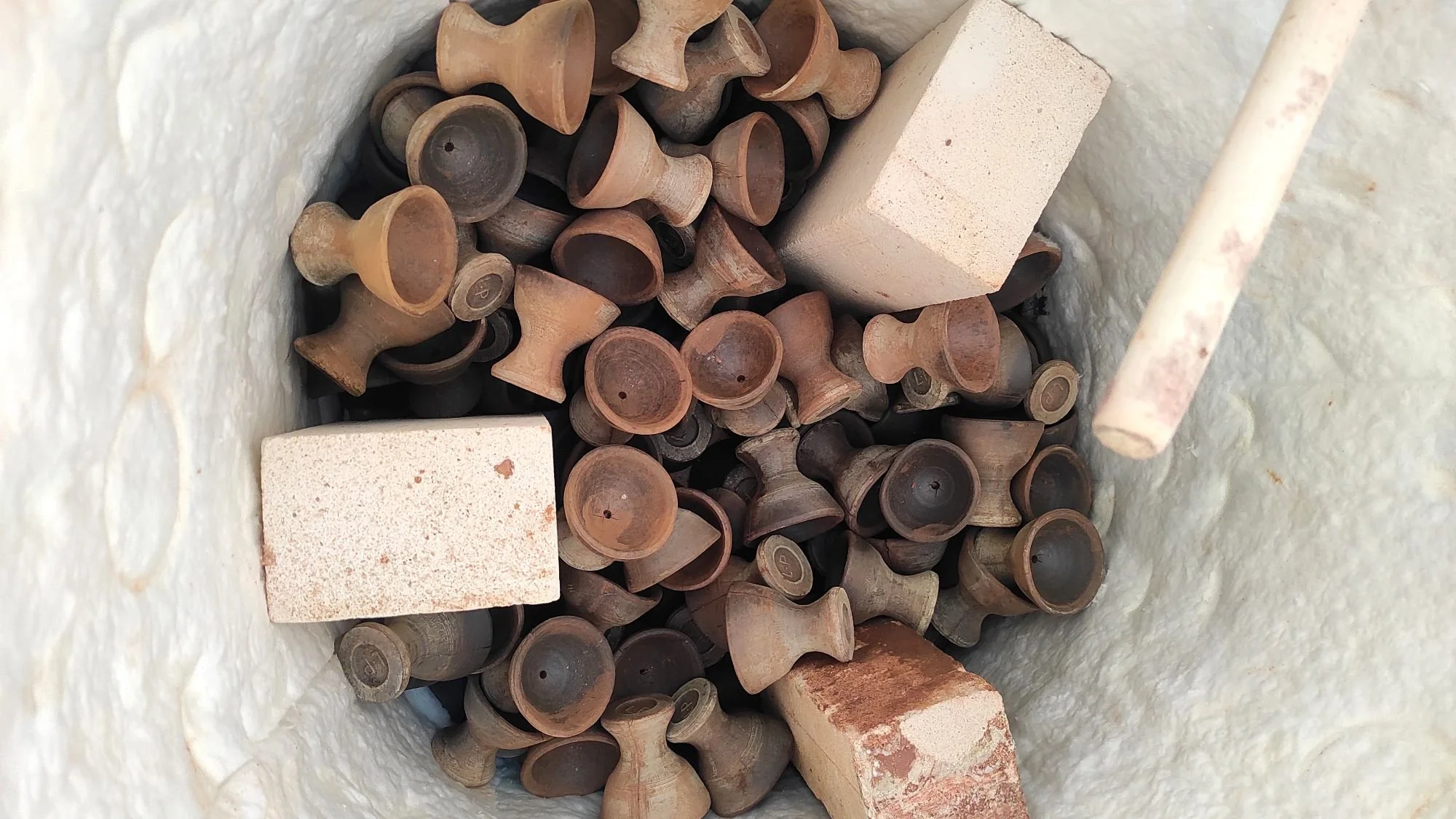 Clay chimney pots and bricks inside a round, white, textured chimney or oven wall.