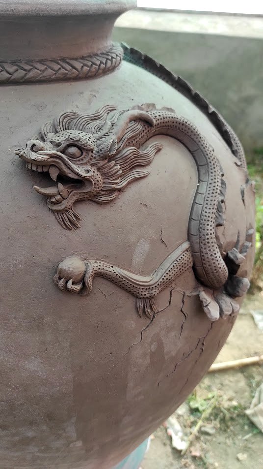 A close-up of a ceramic or clay pot decorated with a raised dragon design in traditional Asian style.