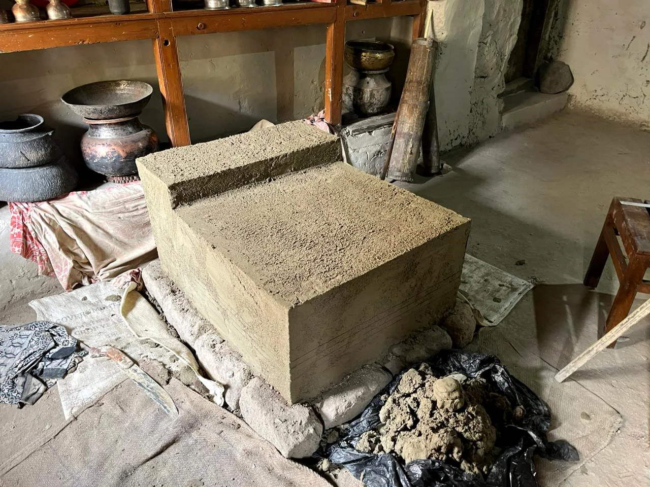 A large rectangular stone block being carved or shaped inside a workshop, with pottery and tools in the background.