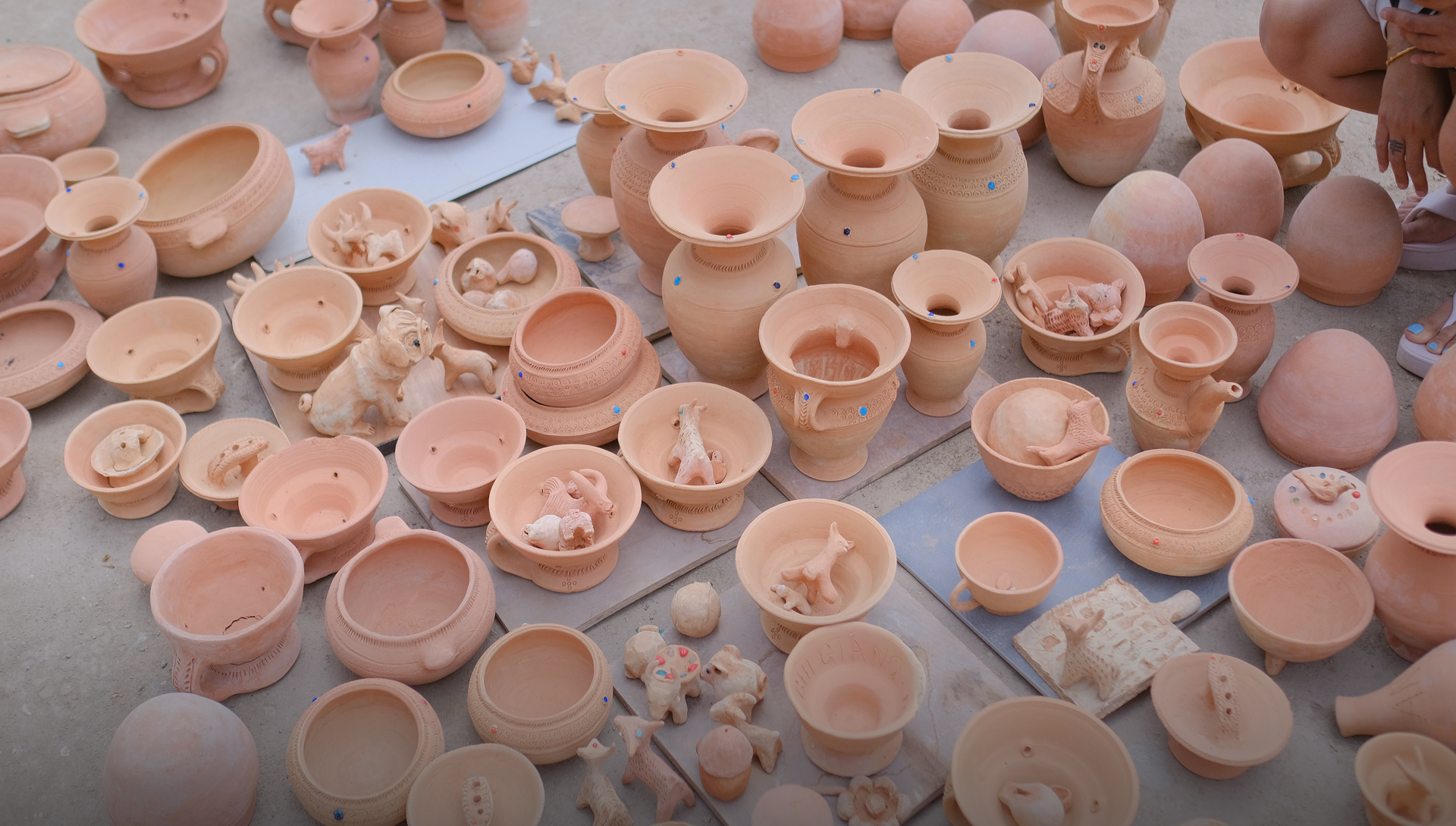 Various unglazed terracotta pottery including bowls, vases, and figurines displayed outdoors on the ground.