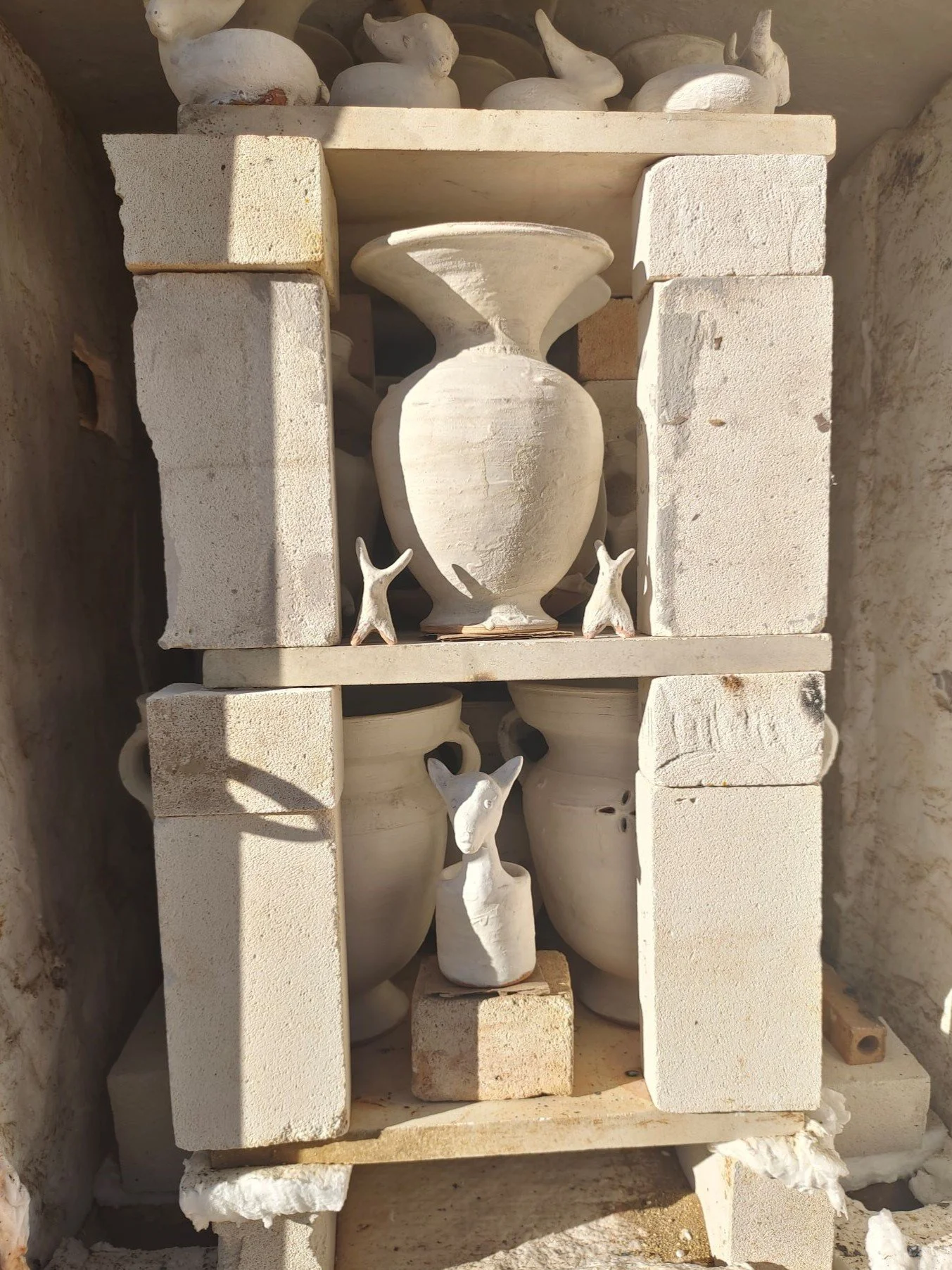 A collection of white ceramic vases and animal figurines arranged on a tiered shelf made of stone blocks, with some figurines resembling ibrx, yaks, and other animals.