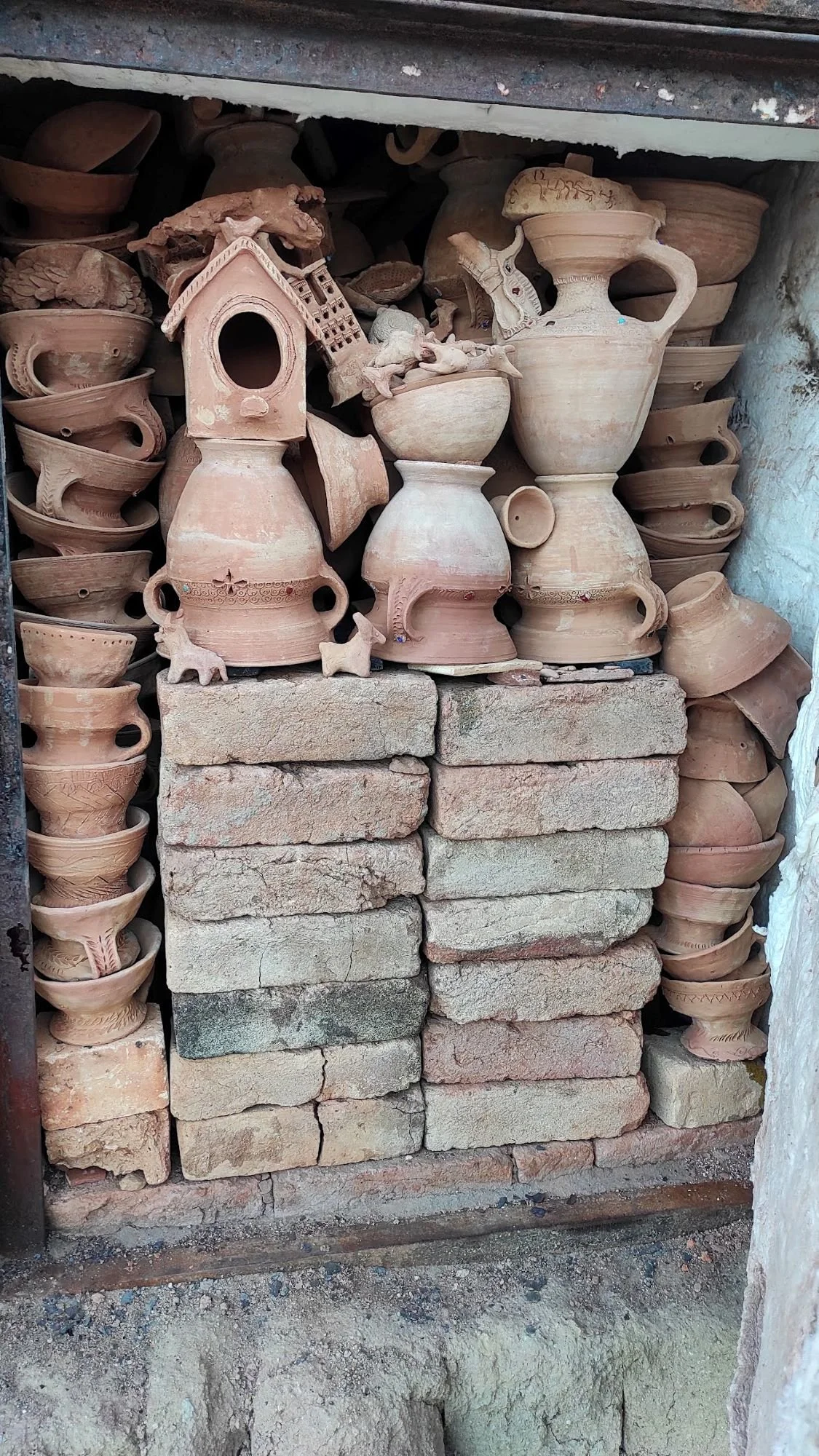 Stacked bricks at the bottom with various clay pottery and decorative vessels above.