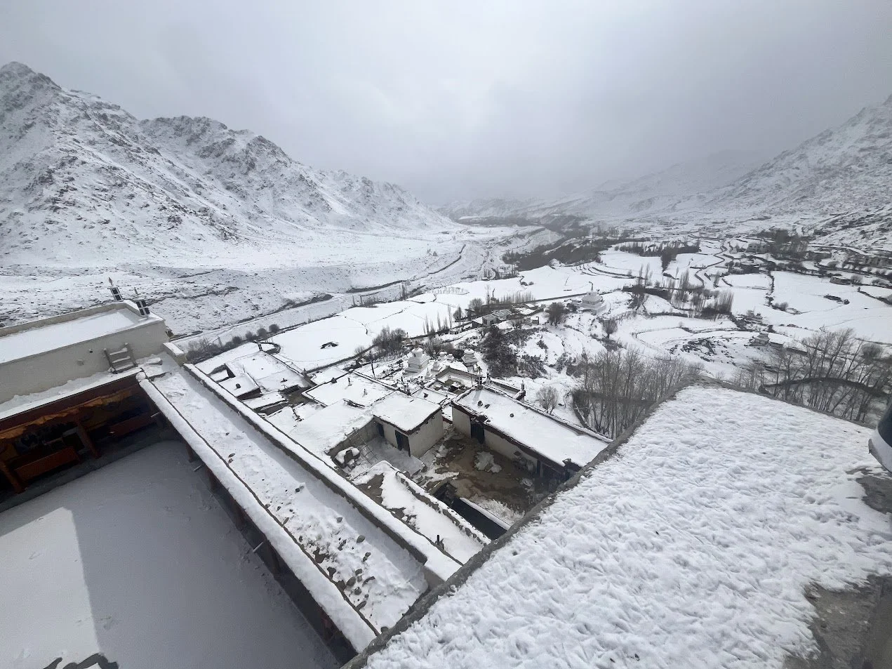 Snow-covered rooftops and a valley surrounded by snow-covered mountains in a rural area.