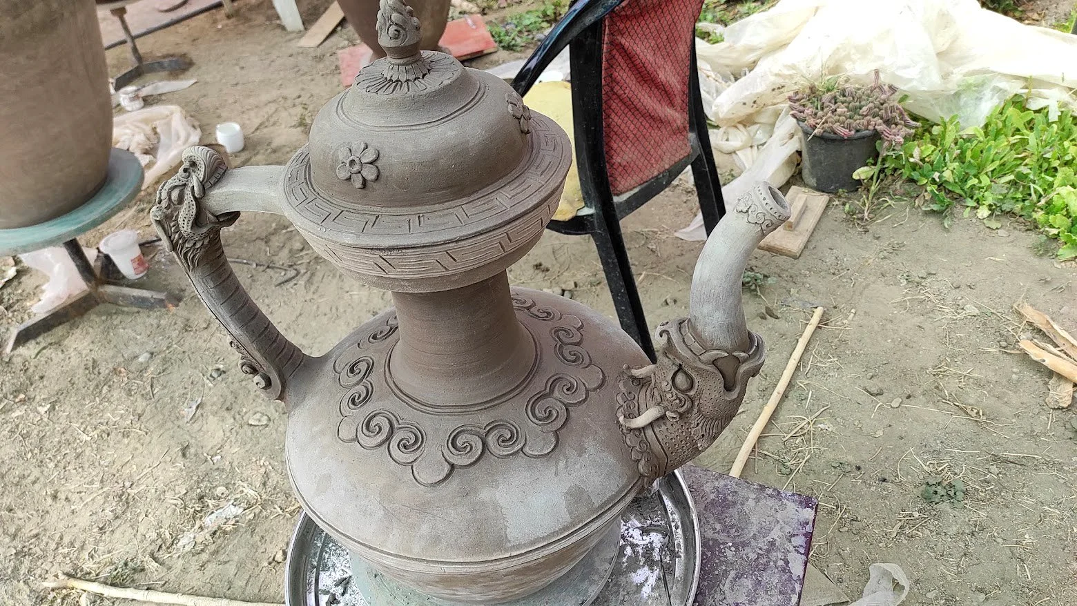 A detailed stone or clay teapot with ornate dragon and floral carvings, placed outdoors on a work surface.