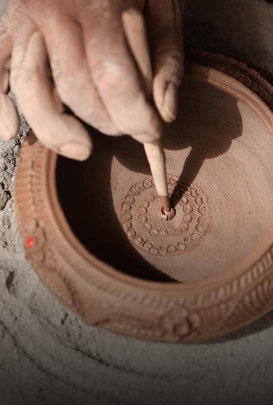 A person drawing patterns inside a clay pot with a pointed tool.