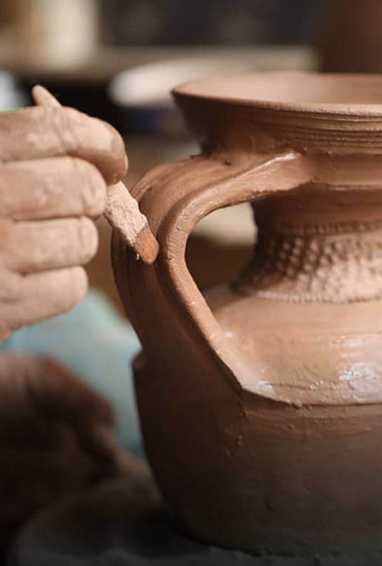 A close-up of hands shaping a clay vessel on a pottery wheel.
