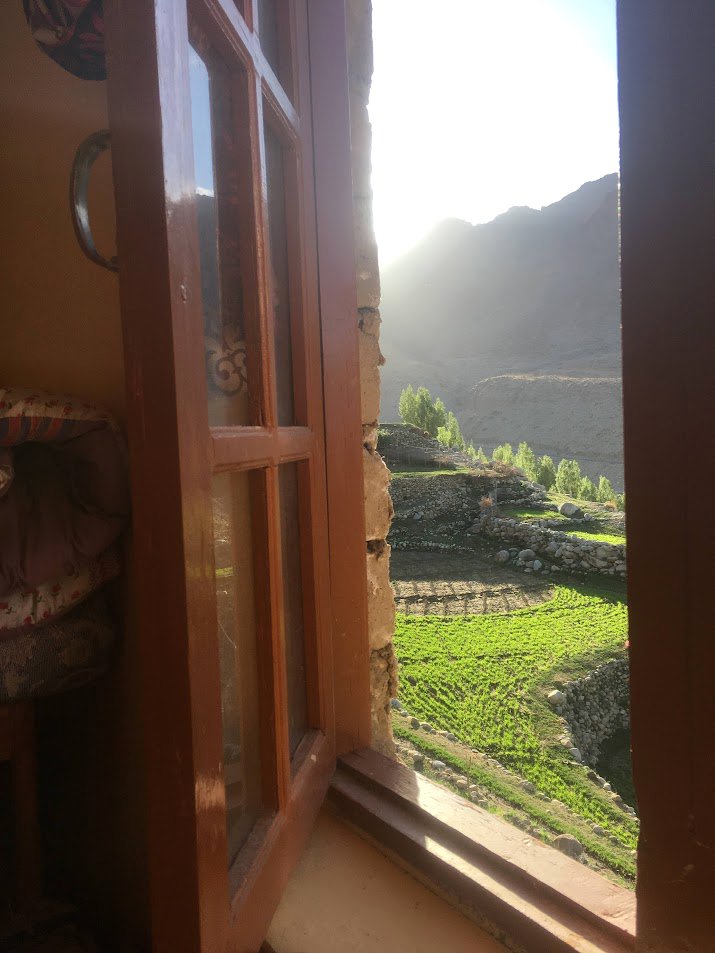 Open window with a view of green terraces and mountains in the distance, sunlight illuminating the scene.