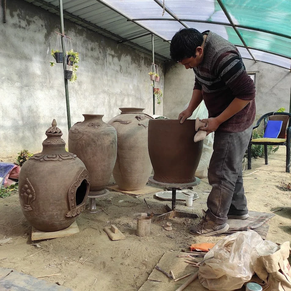 Rigzen namgail working on a large clay pot in a craft studio, surrounded by other finished clay pots.
