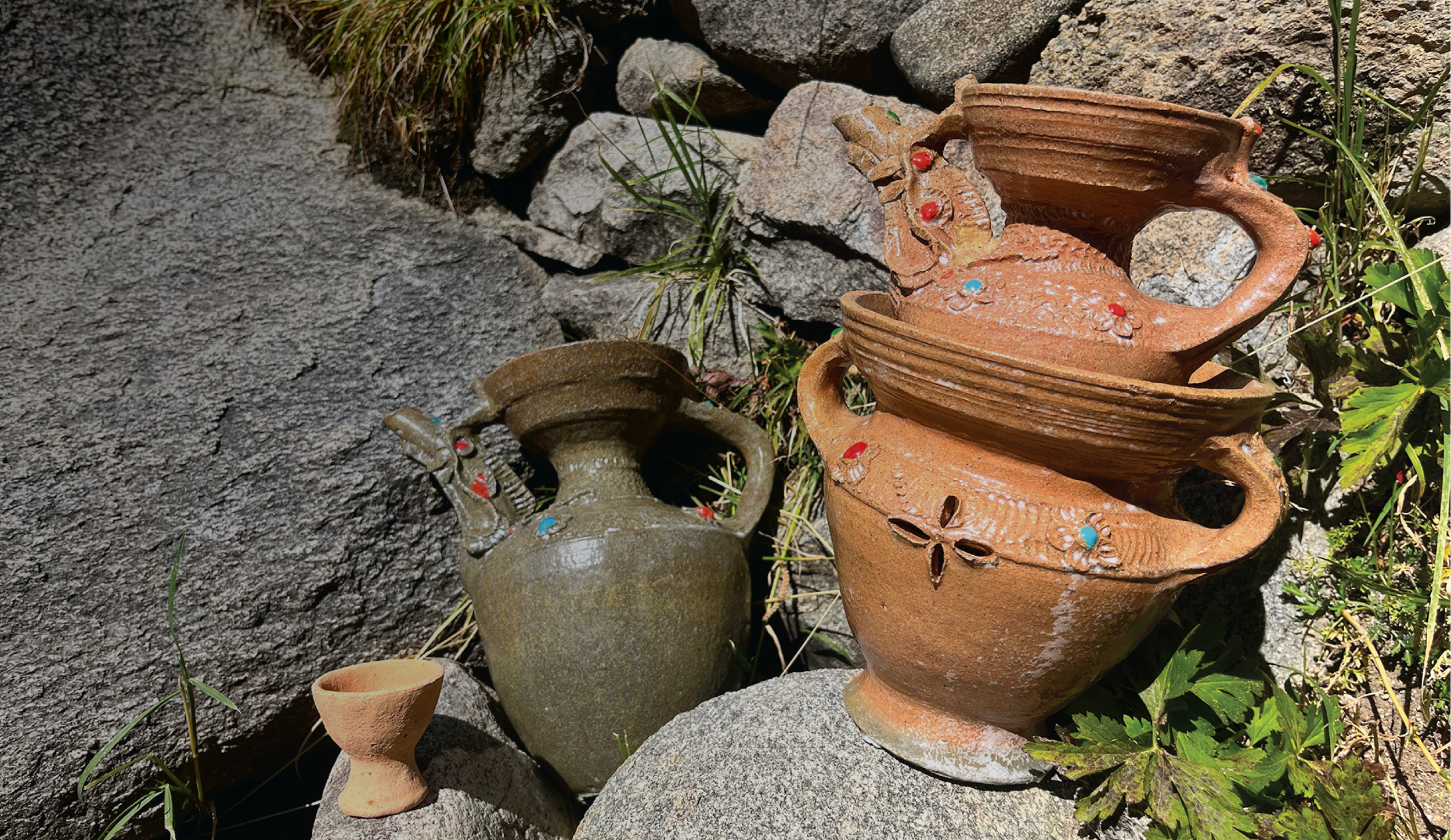 Several decorative clay pots of various sizes and shapes placed among rocks and greenery outdoors.