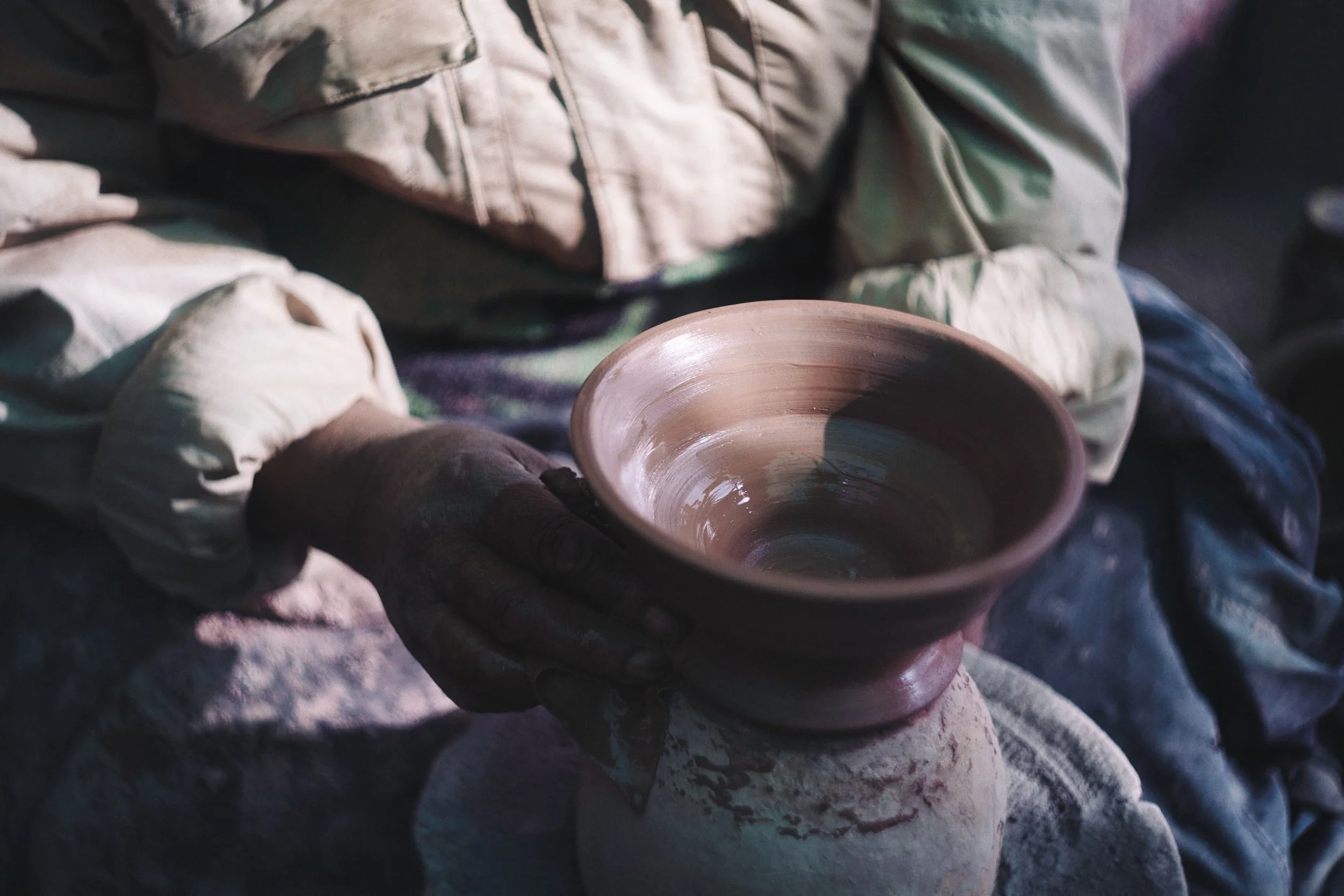 A person shaping a clay bowl on a pottery wheel, wearing a beige shirt.