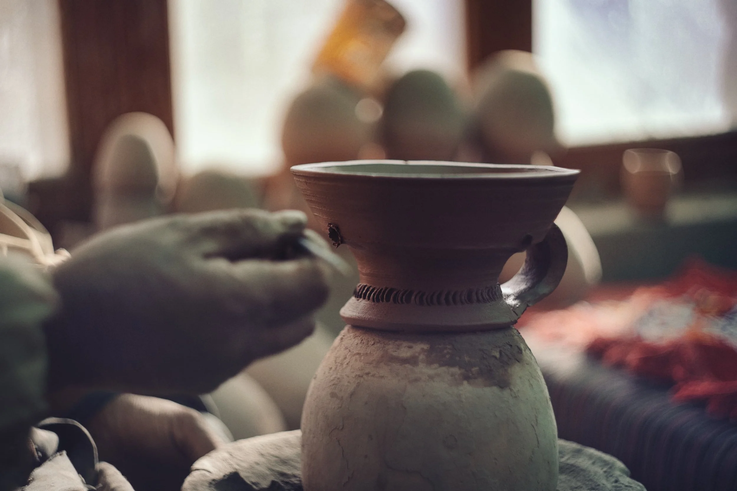Close-up of various clay pottery and vases in a workshop, with a focus on a decorated clay vase in the center, background blurred.