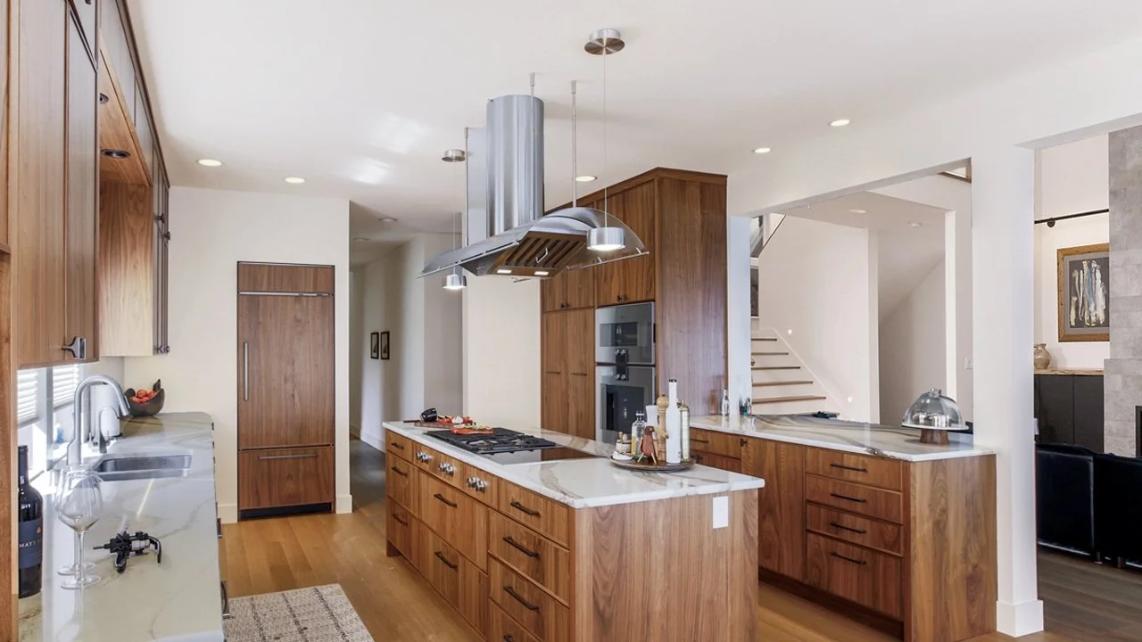 Modern kitchen with wooden cabinets, white marble countertops, stainless steel appliances, and a kitchen island with a range hood.