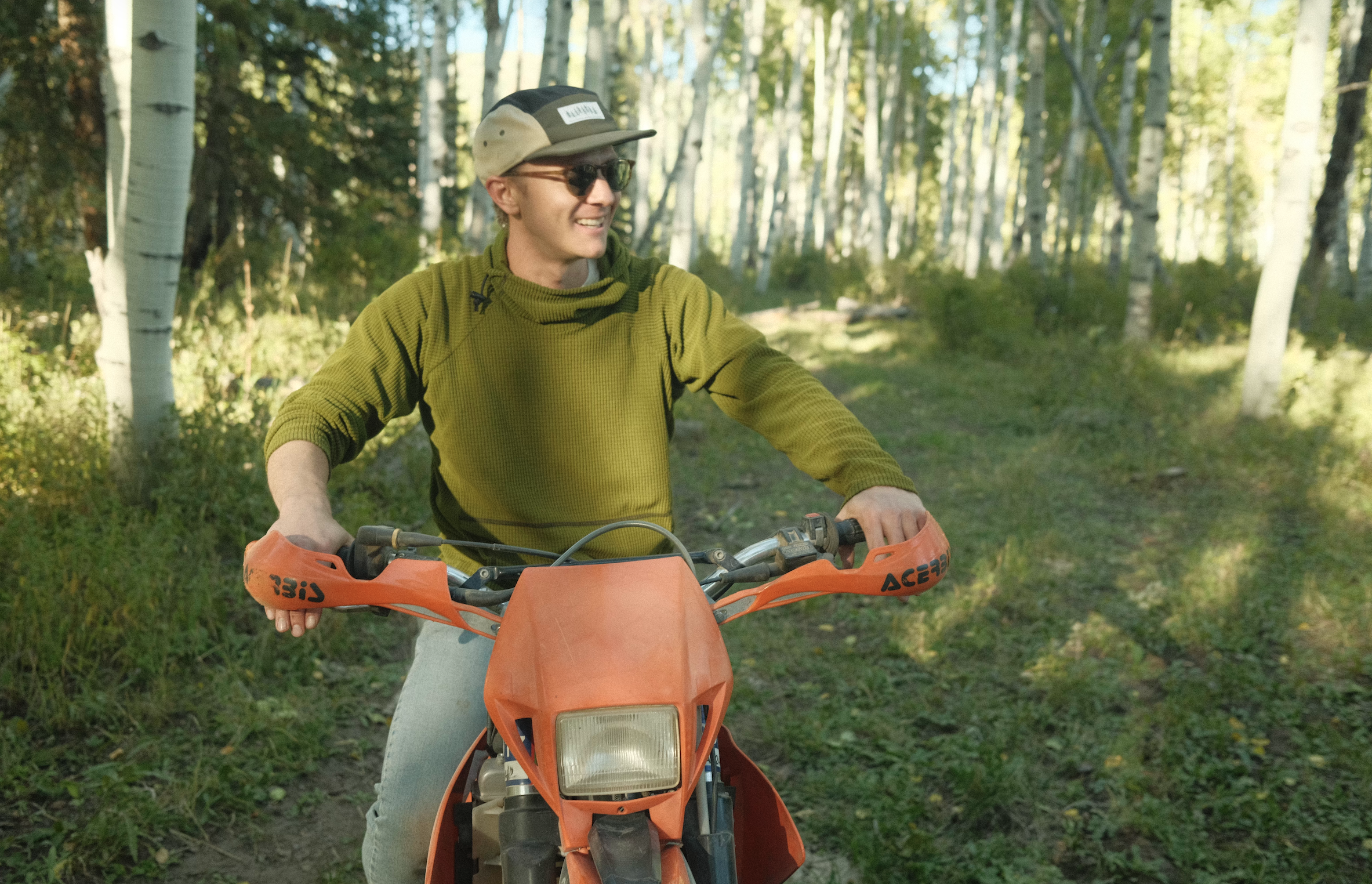 Person riding an orange dirt bike through a forest trail