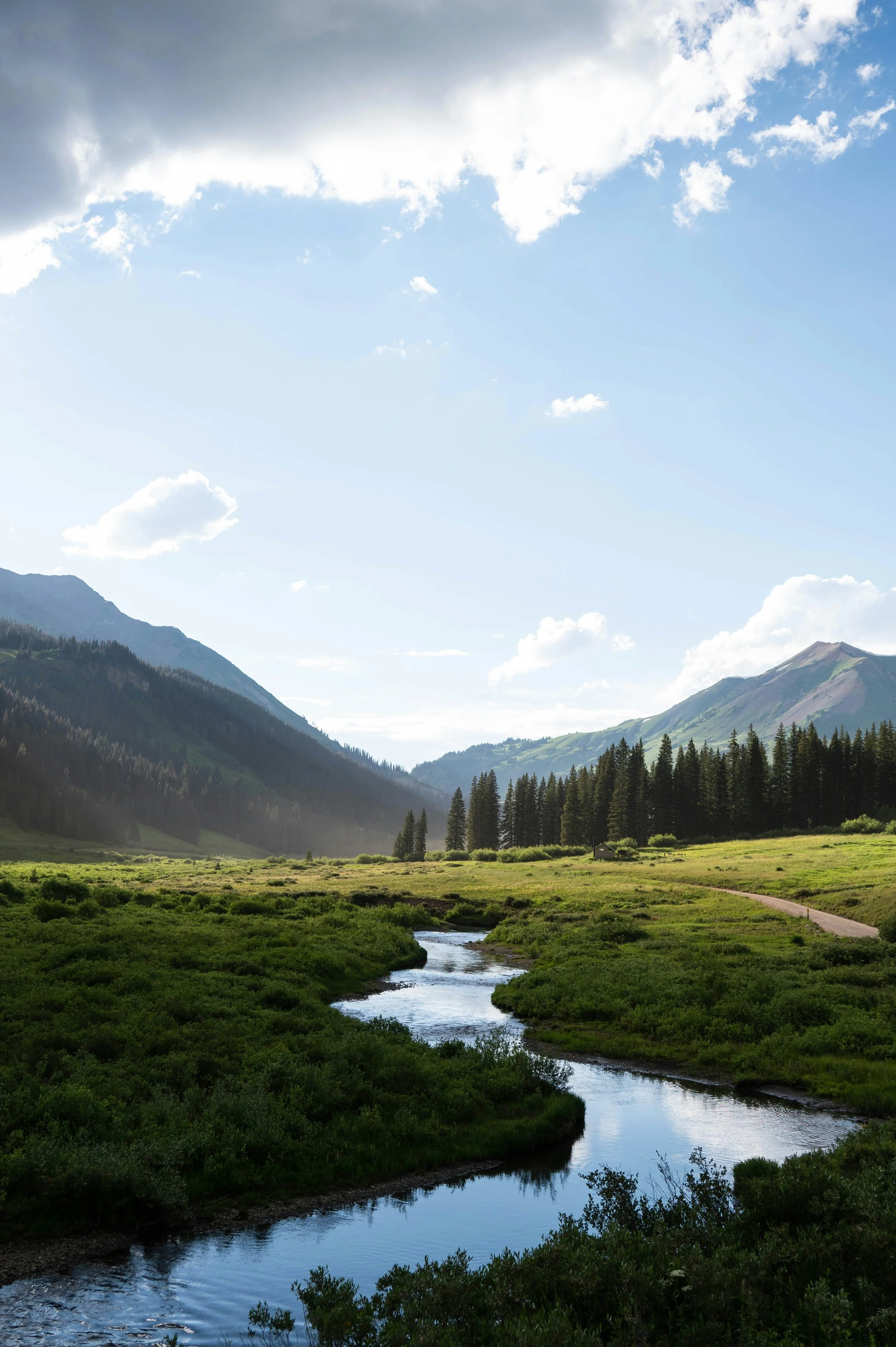 A winding creek through a wide mountain valley in the North Fork Valley, Colorado, with evergreen forest and peaks in the distance