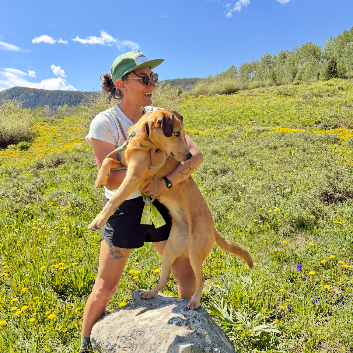 Liza, co-founder of GoodPair Studio, holding her dog in a wildflower meadow in the Colorado mountains