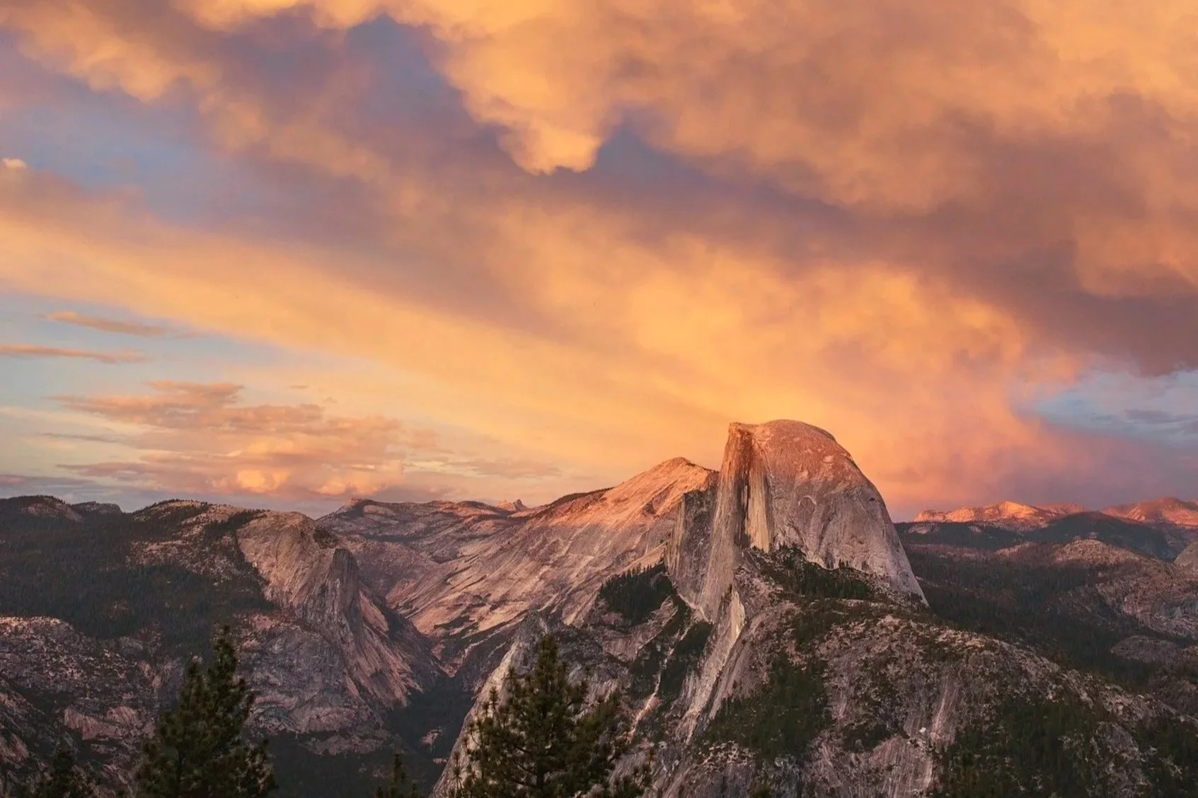 Sunset over Half Dome in Yosemite National Park with colorful clouds in the sky and rugged mountain landscape