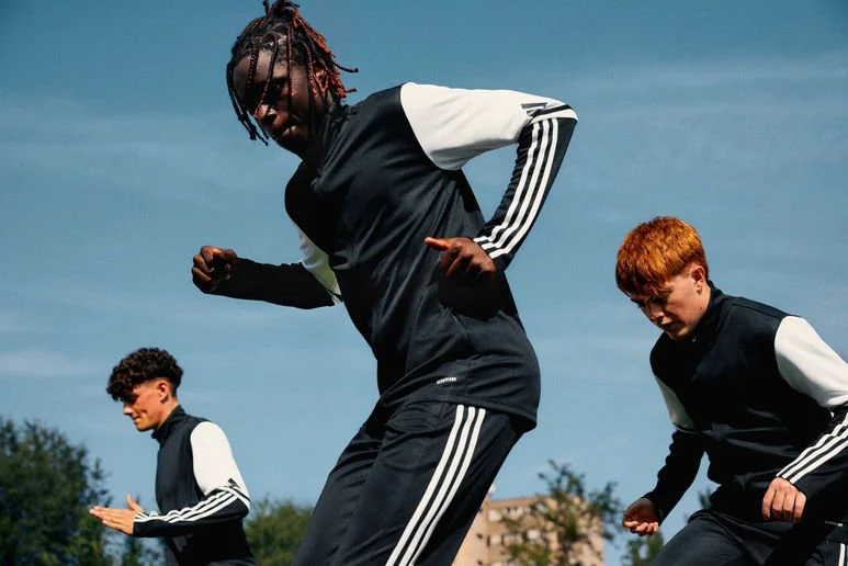 Three young people in athletic clothing stretching outdoors on a sunny day.