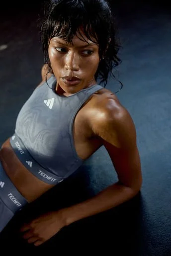 Athletic woman lying on the floor in workout attire, looking to the side against a dark background.