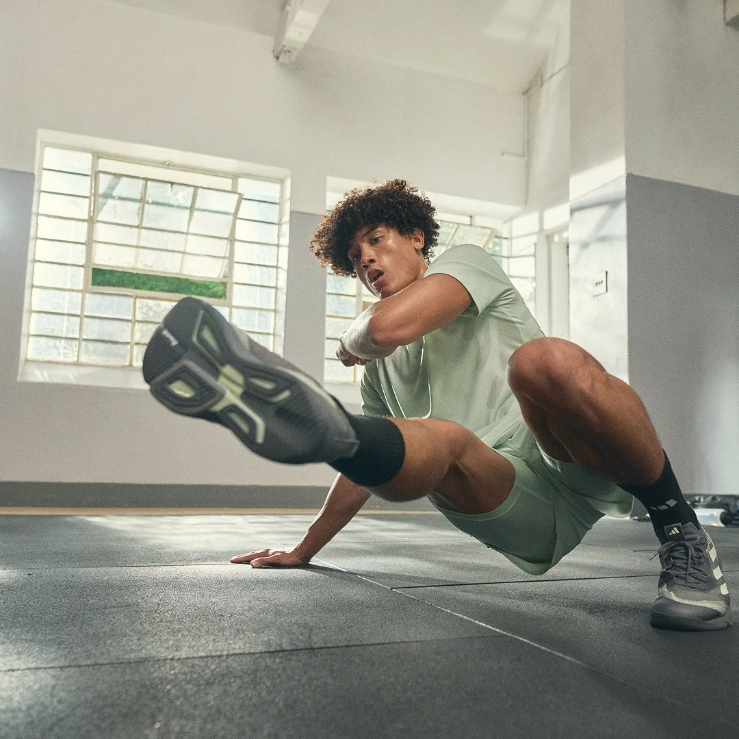A man with curly hair in sportswear doing a floor exercise in a gym with large windows.